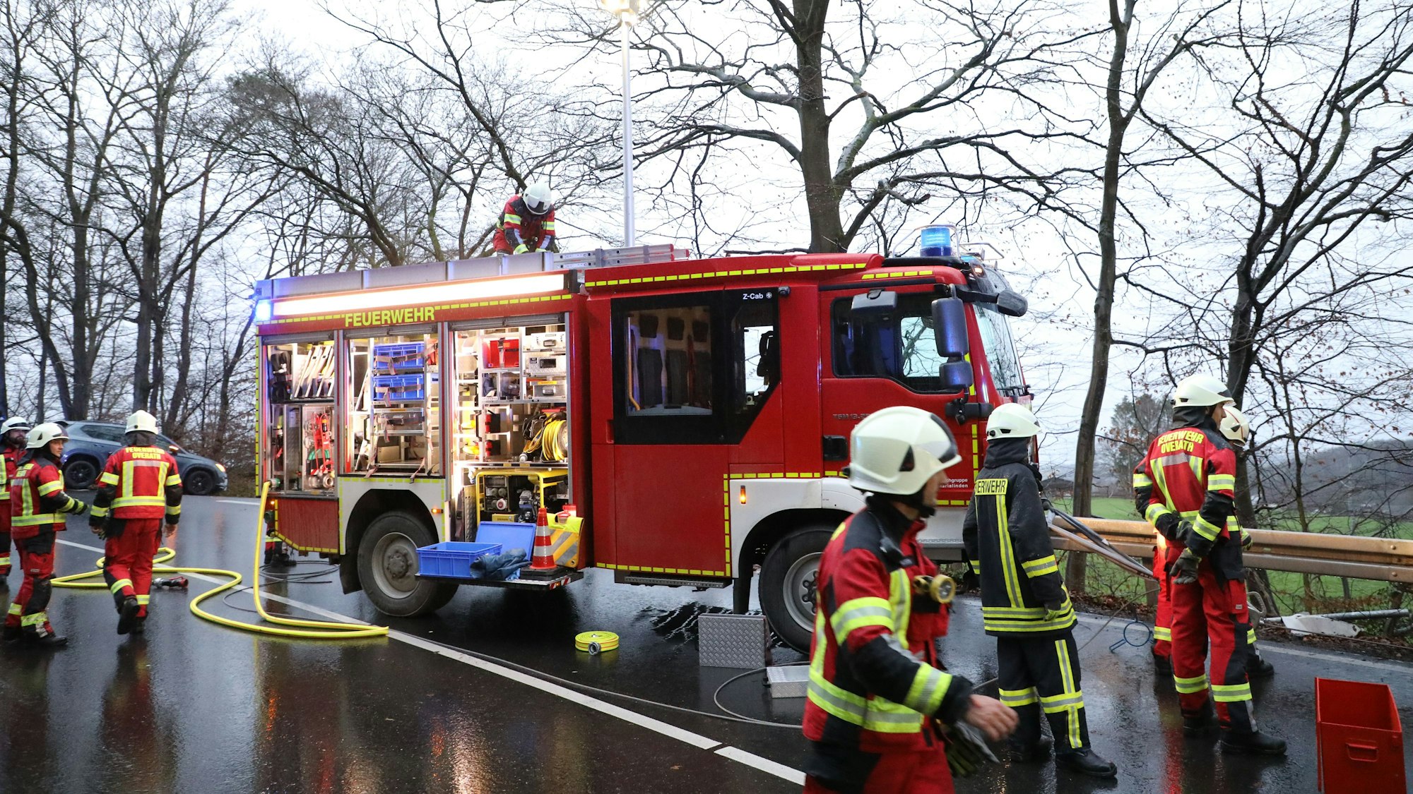 Ein Feuerwehrfahrzeug steht auf einer Landstraße, Feuerwehrmänner entnehmen dem Wagen Schläuche.
