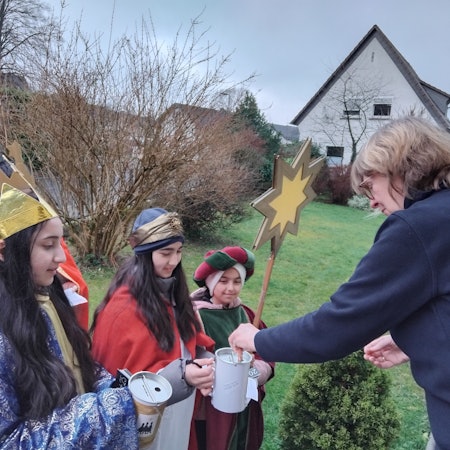 Eine Frau steckt einen Geldschein in die Sammeldose von Sternsingern