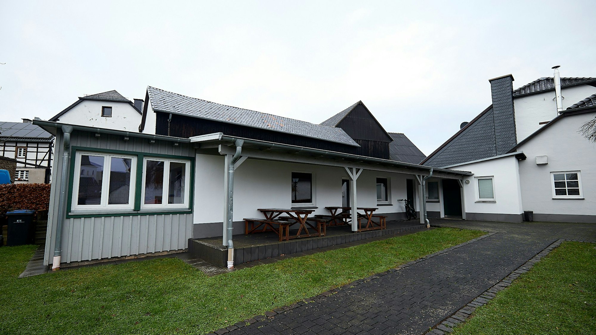 Auf der Terrasse vor einem weißen Gebäude stehen Tische und Bänke.