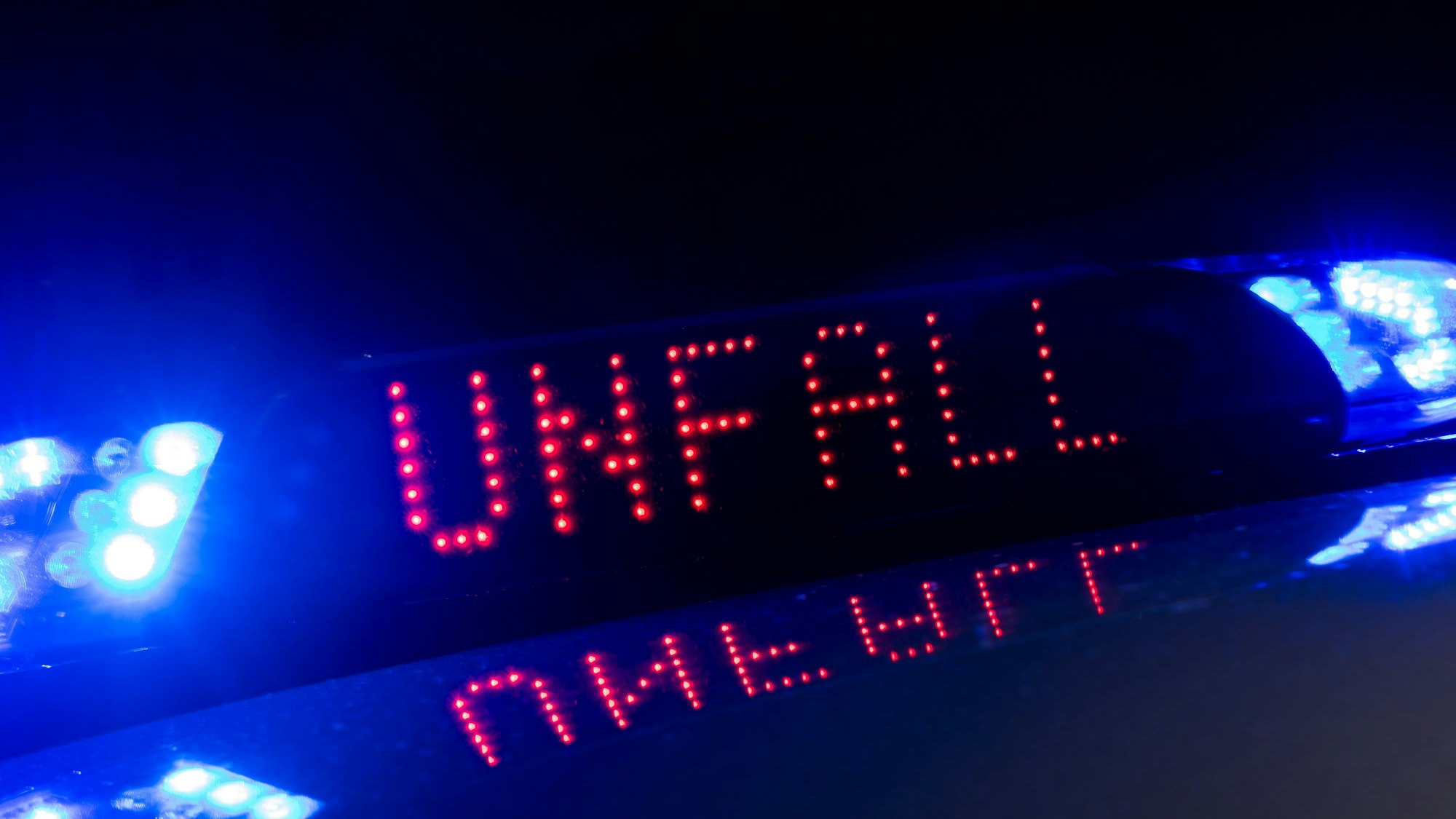Das Blaulicht auf einem Fahrzeug der Polizei leuchtet in der Dunkelheit, während auf dem Display der Hinweis „Unfall“ zu lesen ist.