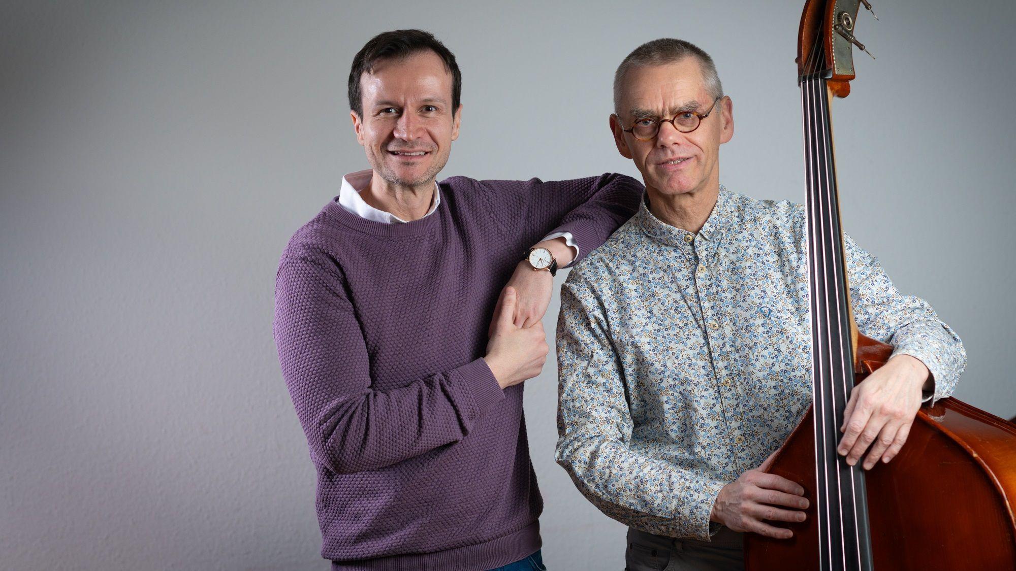 Auf dem Bild stehen zwei Männer nebeneinander. Einer von ihnen hält ein Kontrabass in den Händen.