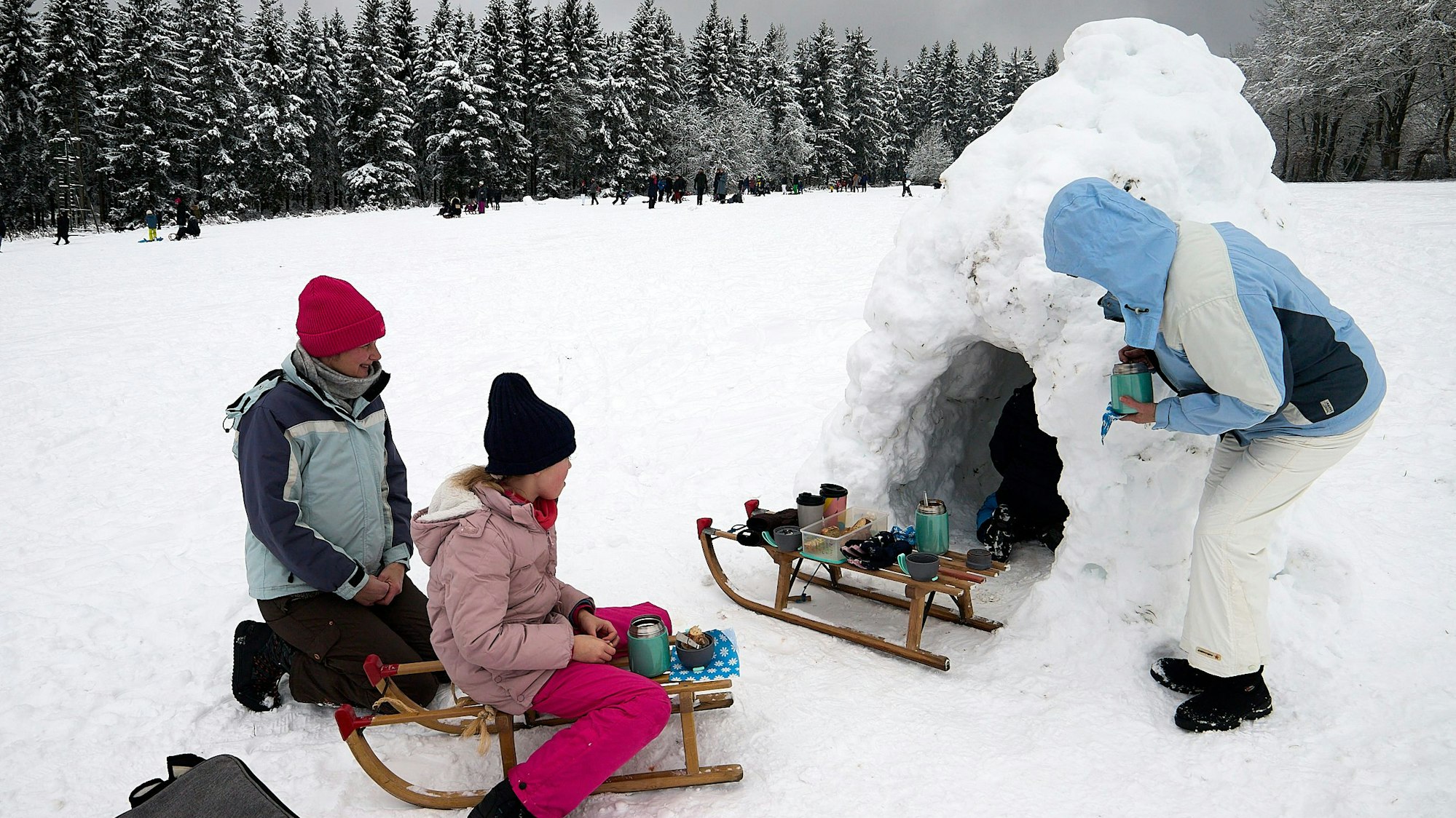 Die Familie hat es sich an der Eishöhle bequem gemacht, auf einem der beiden Schlitten stehen Getränke bereit.