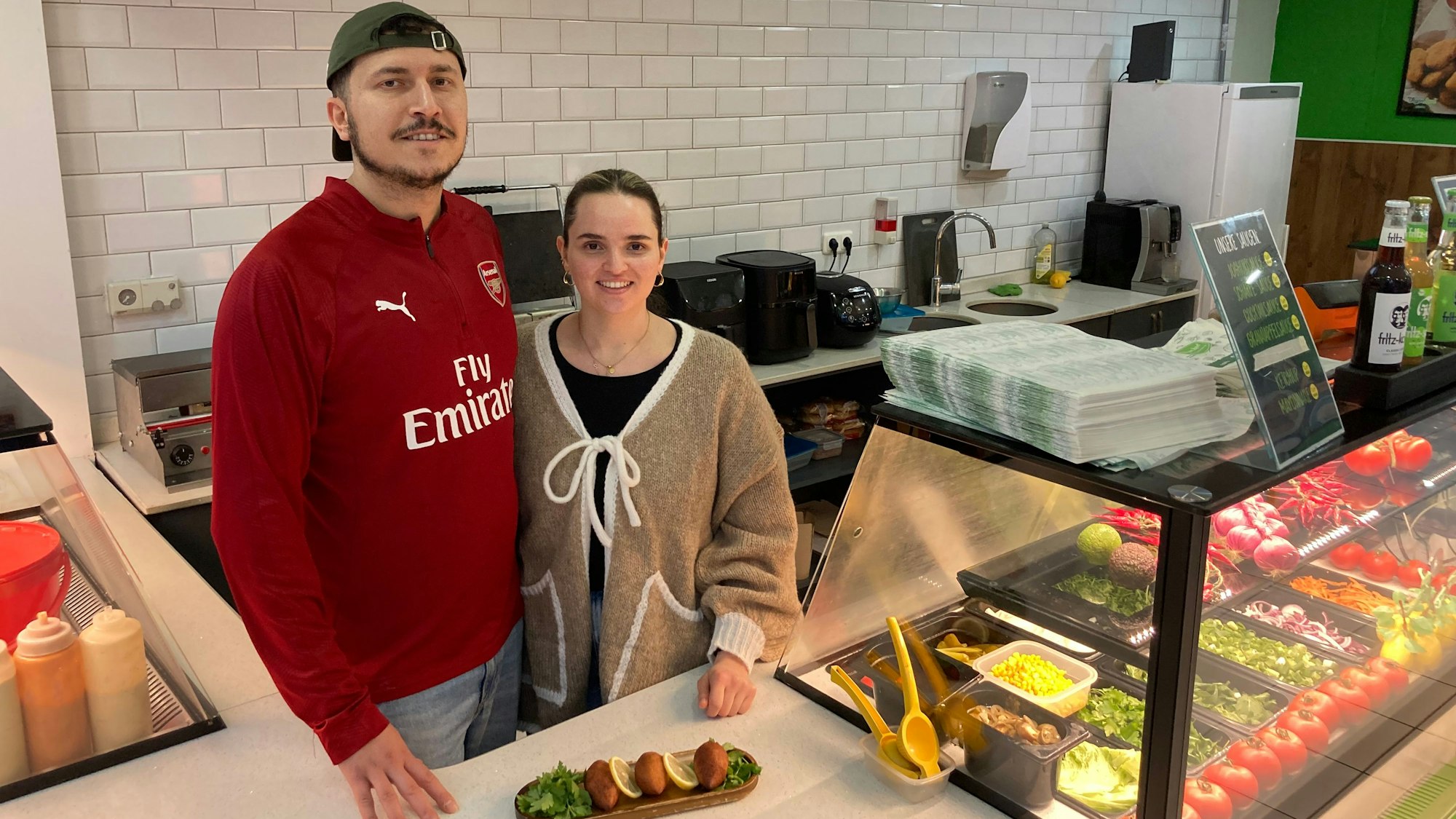 Ein Mann mit Kappe und eine Frau stehen hinter einer Theke, auf der İçli köfte angerichtet wurden.