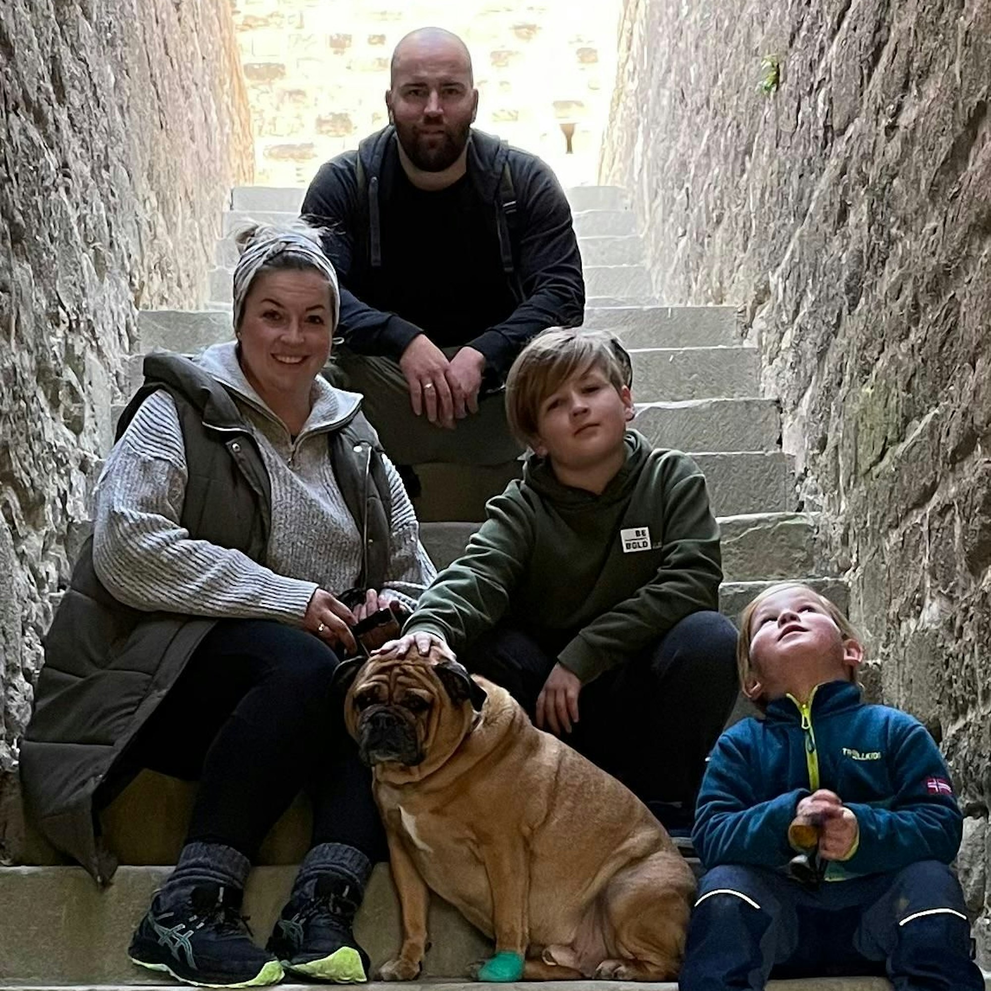 Eine Familie und ihr Hund sitzen für ein Gruppenfoto auf einer Treppe einer alten Burg.