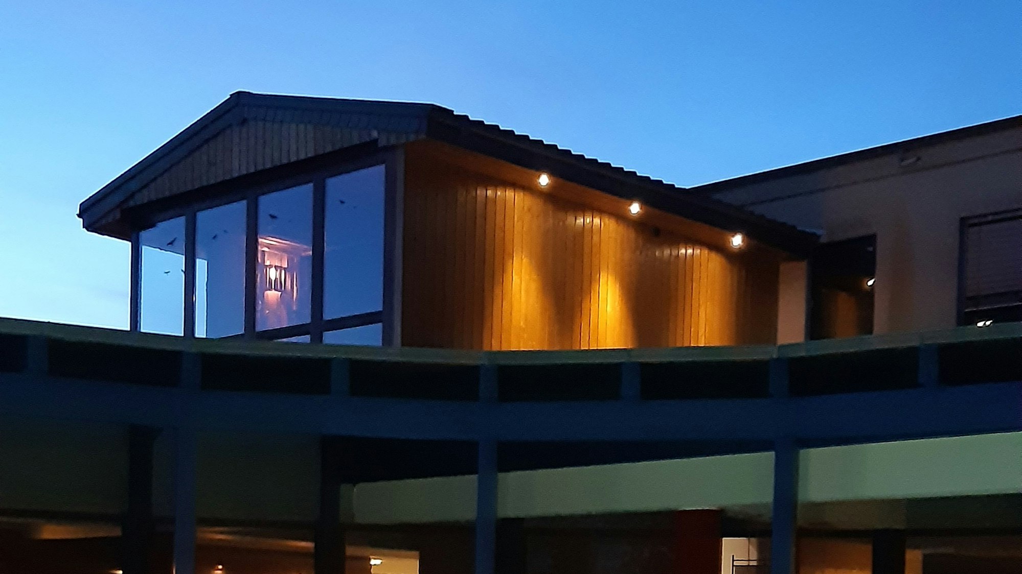 Eine Sauna, die unter dem Dach eines Gebäudes von außen zu sehen ist mit großer Fensterfront