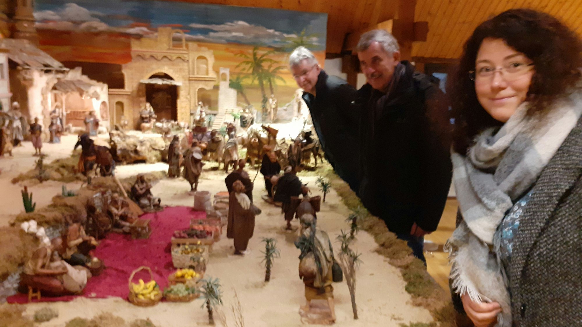 Männer und eine Frau stehen vor einer großen Krippendarstellung.