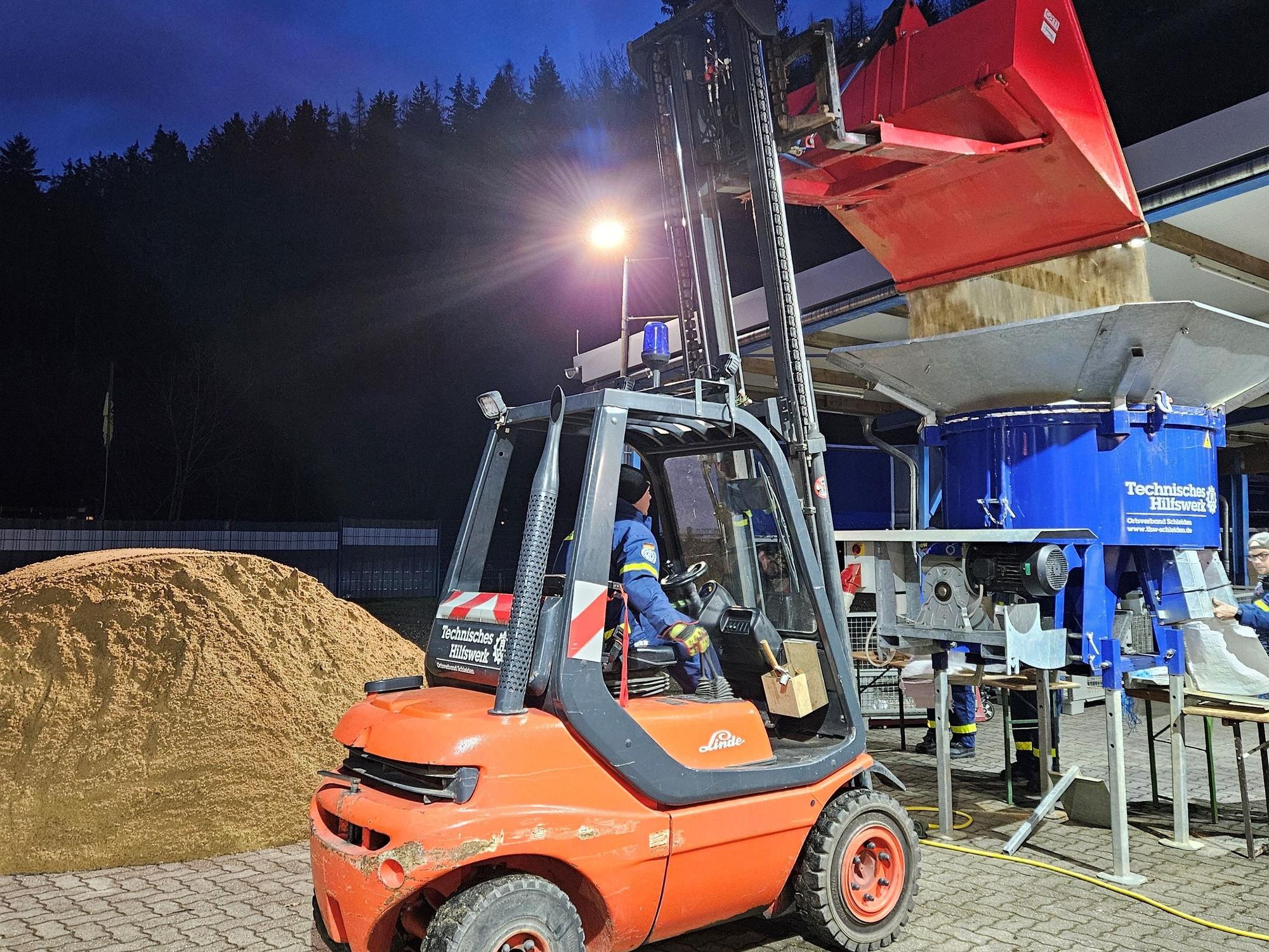 Das Bild zeigt einen Gabelstapler, der Sand in die Sandsackfüllmaschine kippt.