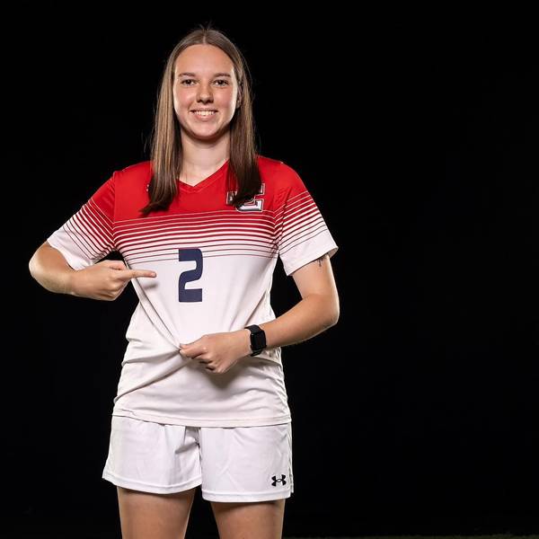 Lena Kücken trägt das Trikot mit der Nummer 2 des Jefferson College. Mit einem Finger zeigt sie auf die Nummer, mit der anderen Hand zieht sie das Trikot straff.