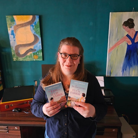 Jana Engel aus Kall steht vor ihrem Schreibtisch und hält die beiden Bücher der Tuchindustrie-Reihe in den Händen.