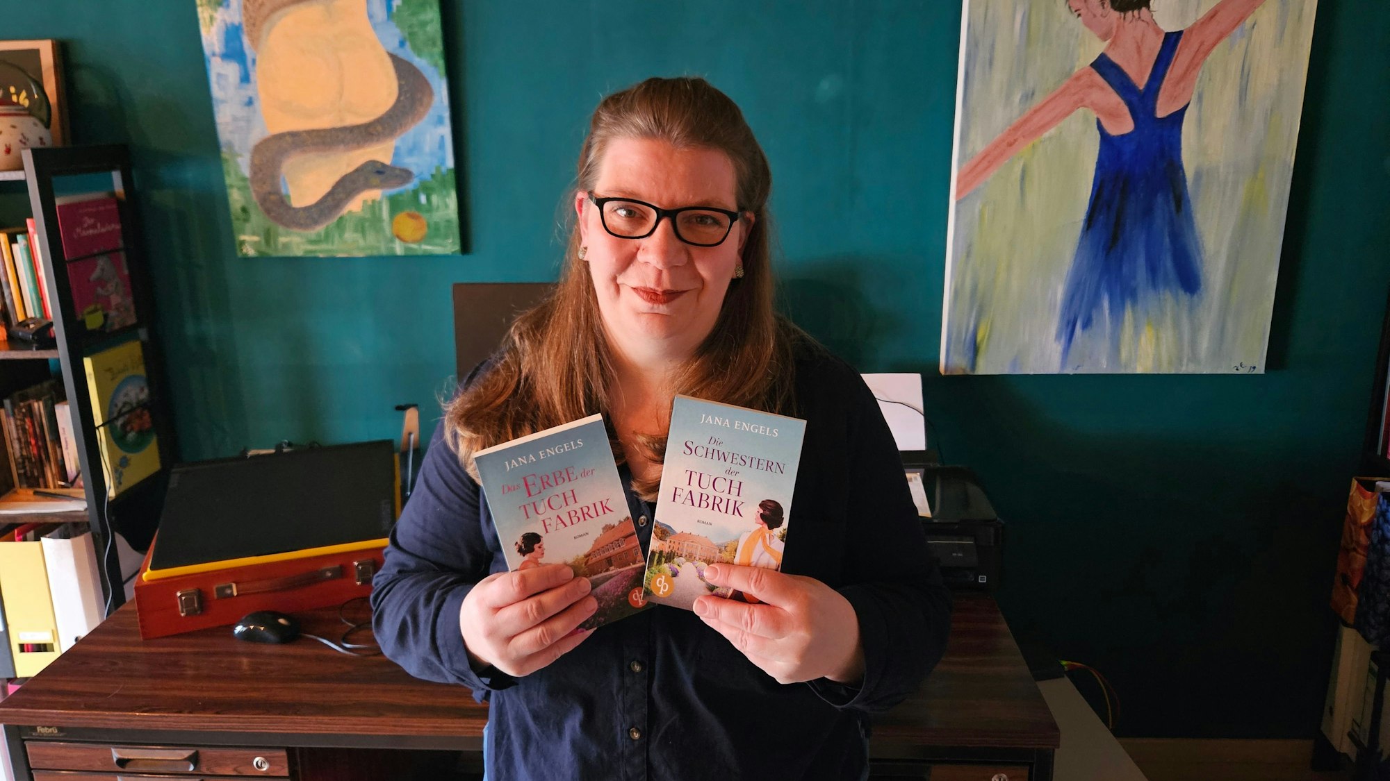 Jana Engel aus Kall steht vor ihrem Schreibtisch und hält die beiden Bücher der Tuchindustrie-Reihe in den Händen.