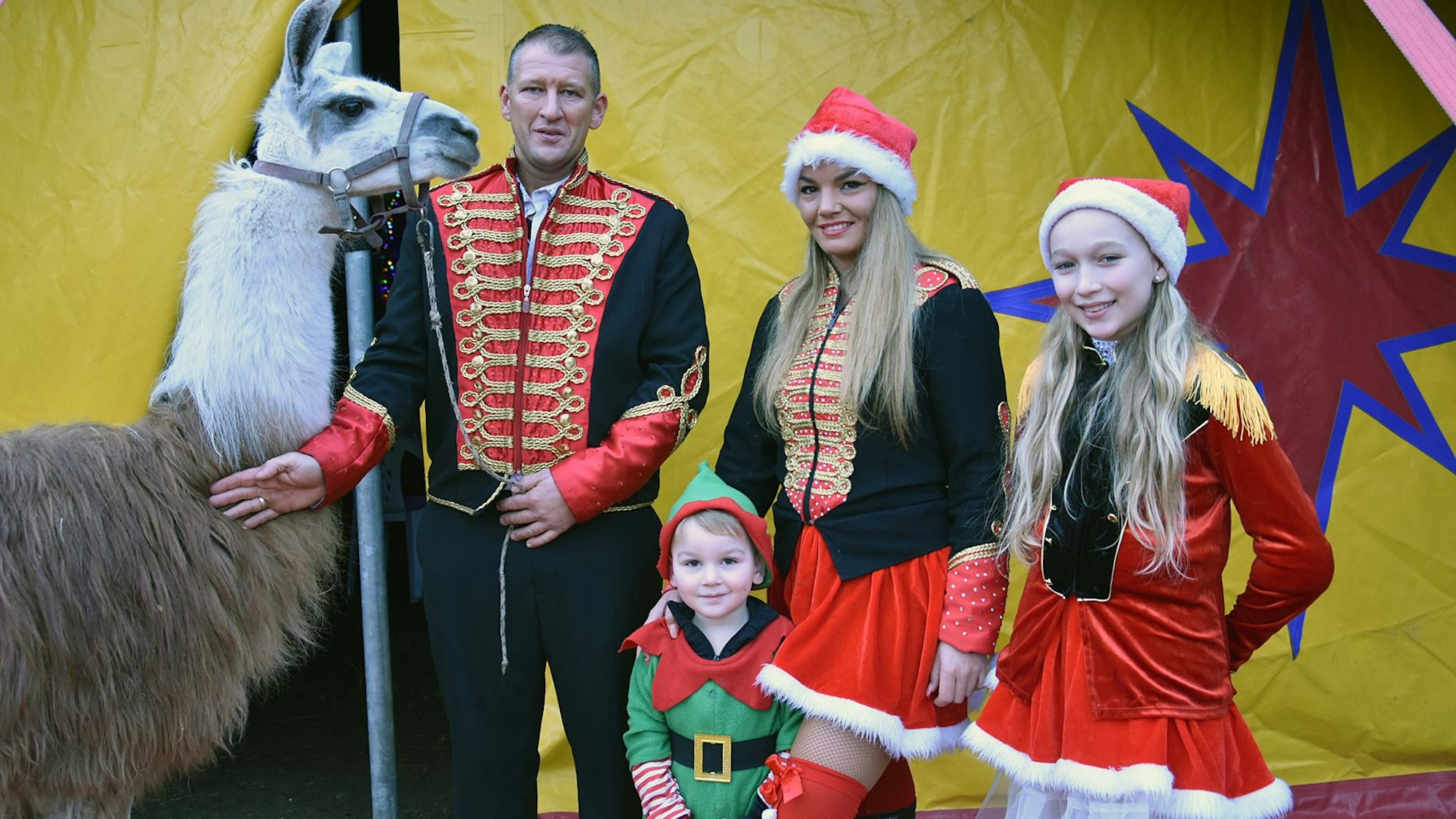 Eine Zirkusfamilie steht mit einem Lama vor einem Zirkuszelt.