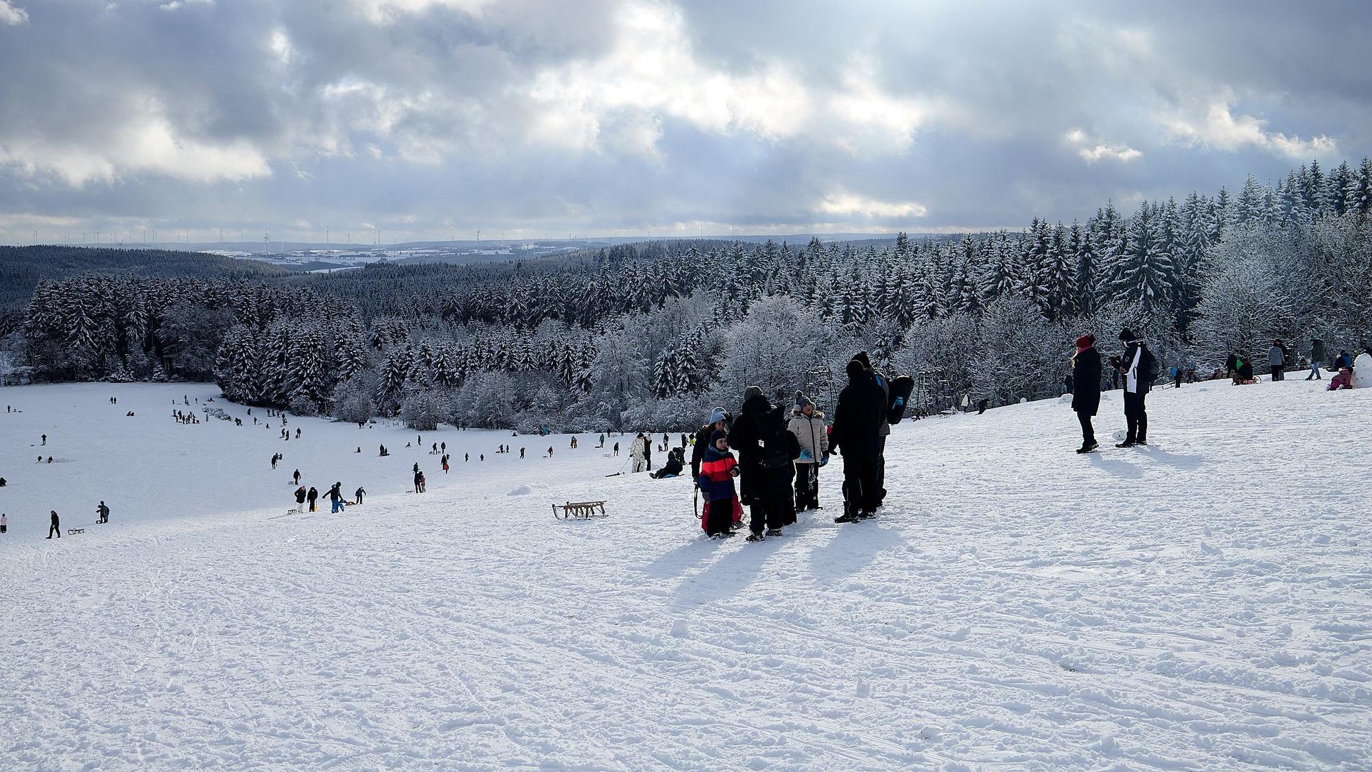Personen auf einer Rodelpiste am Weißen Stein bei geschlossener Schneedecke.