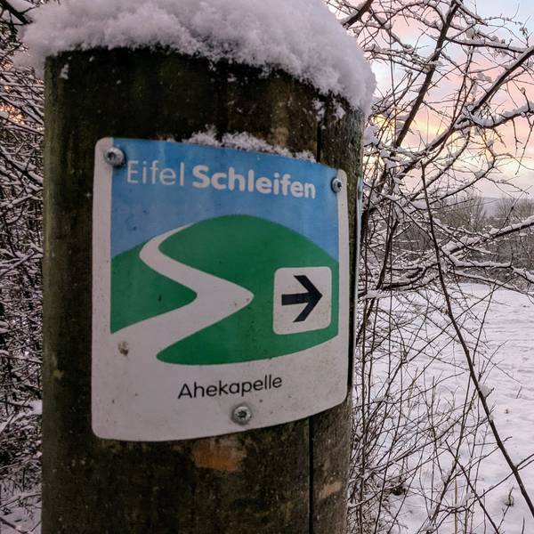 Eine Spaziergängerin mit Hund auf der verschneiten Eifelschleife Ahekapelle im Genfbachtal bei Nettersheim.