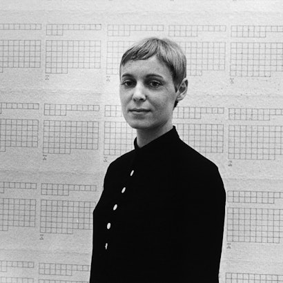 Hanne Darboven steht vor einer Tapete mit leeren Kästchen.