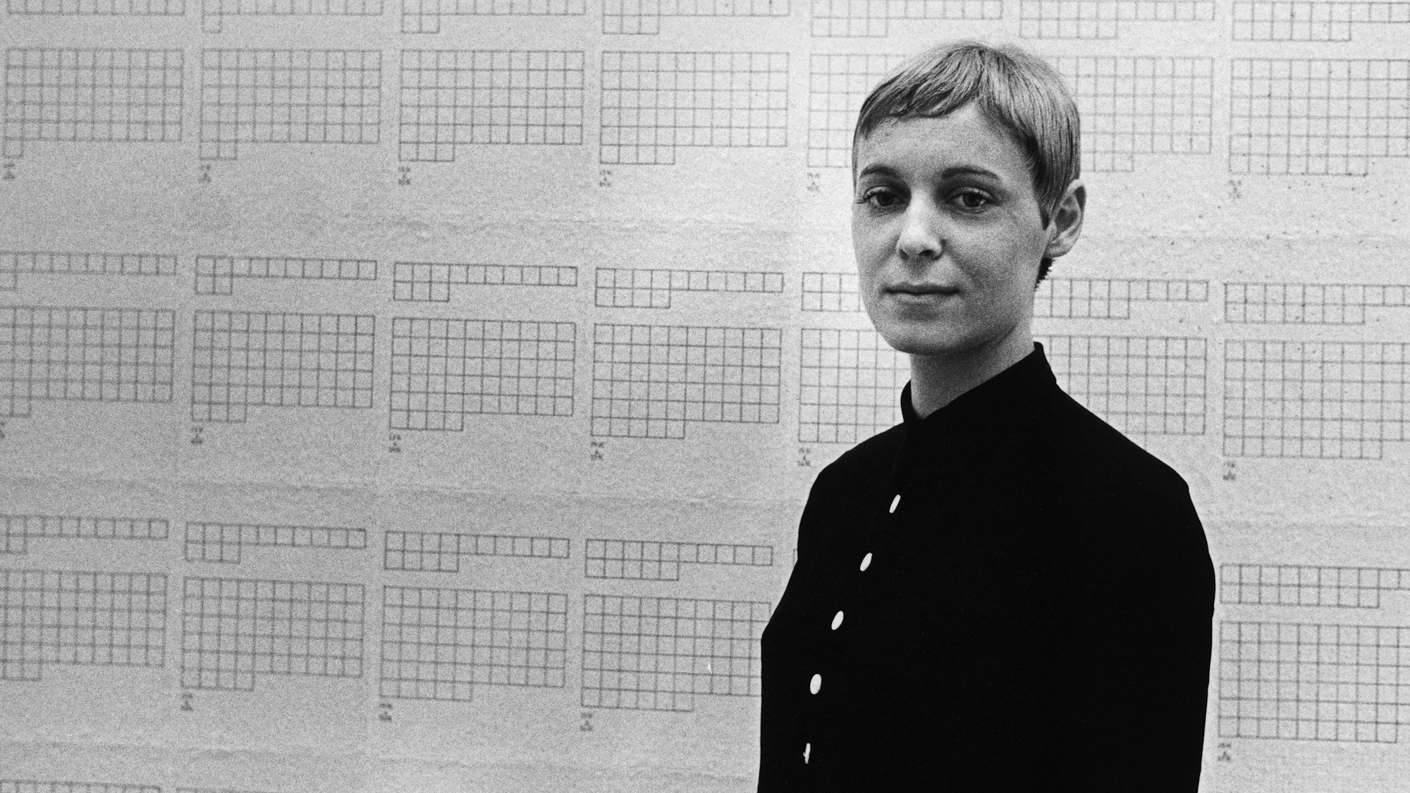 Hanne Darboven steht vor einer Tapete mit leeren Kästchen.