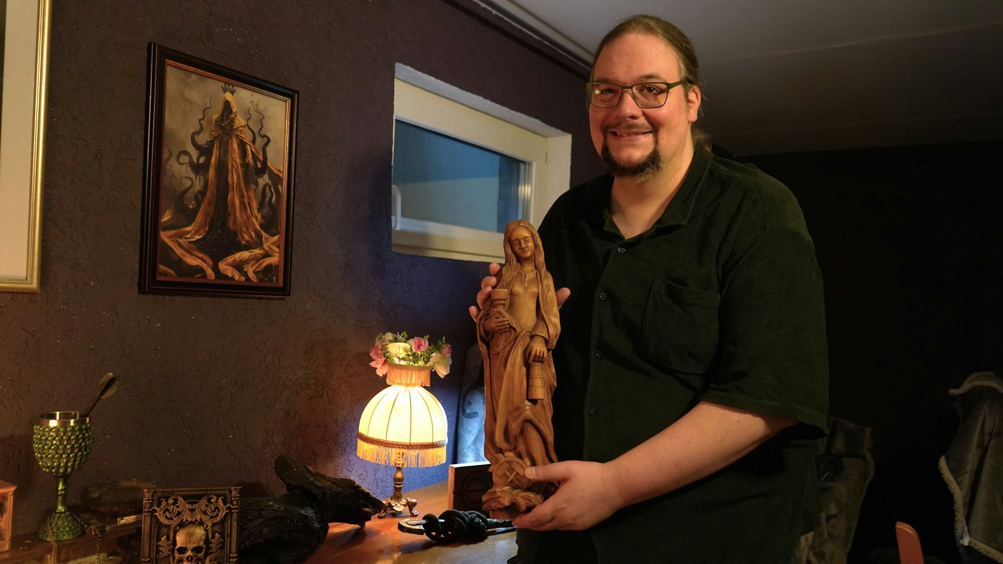 Das Foto zeigt einen Mann, der eine Holzstatue hält.