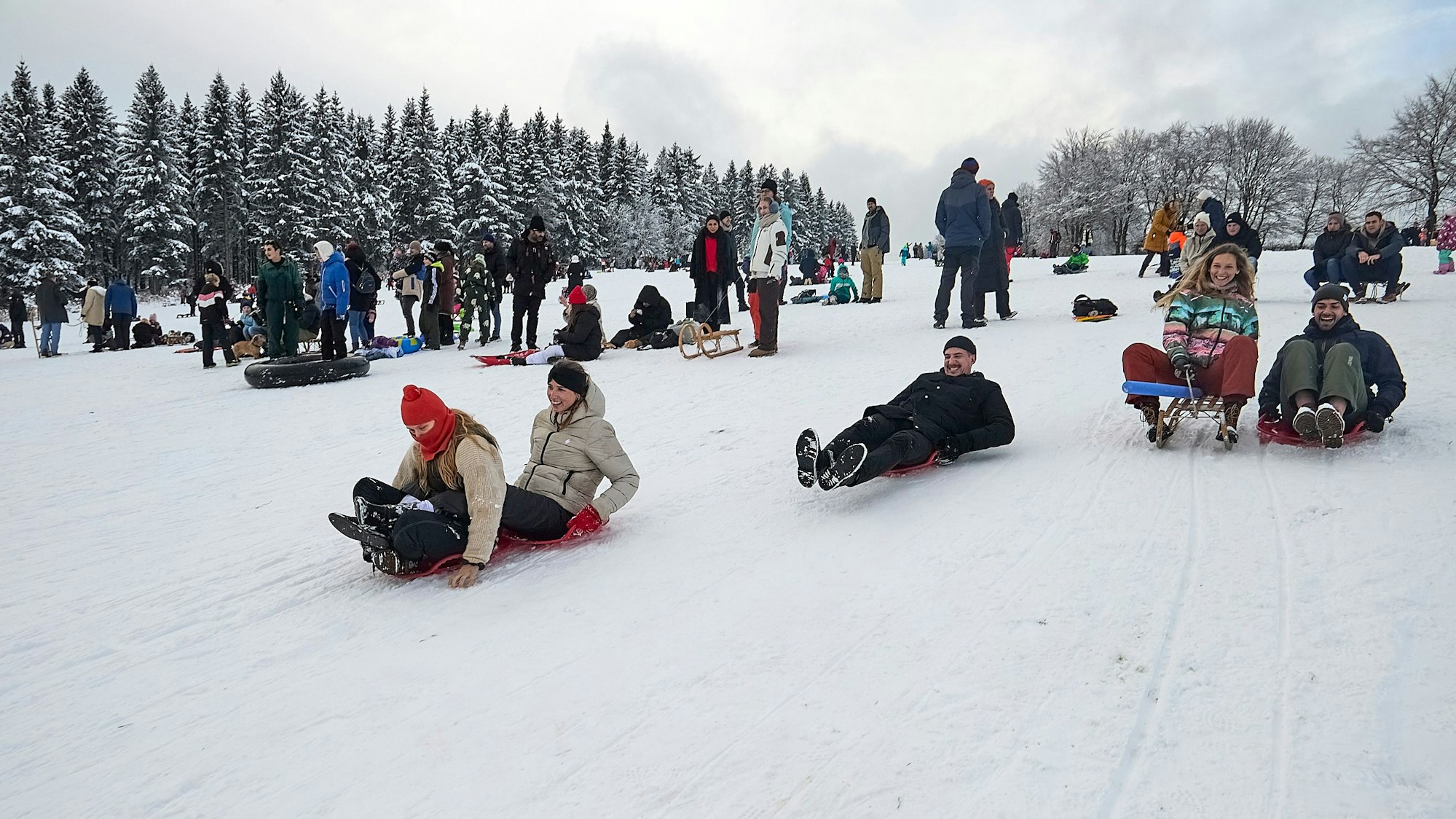 Mehrere Personen rodeln auf Schlitten den Berg am Weißen Stein hinab.