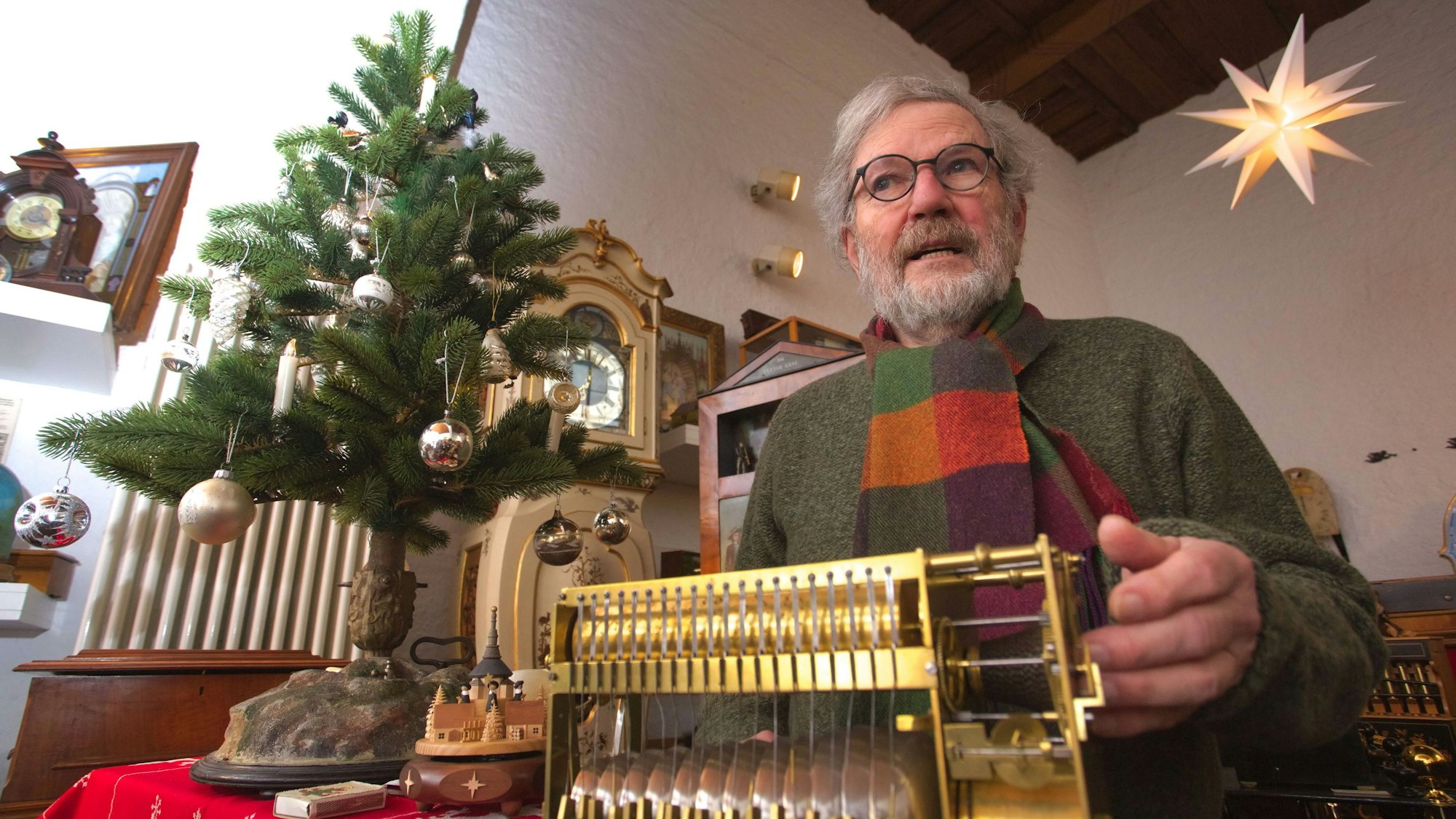 Ullrich Wimmer sitzt hinter einem mechanischen Musikinstrument, eine Hand hat er an der Kurbel.