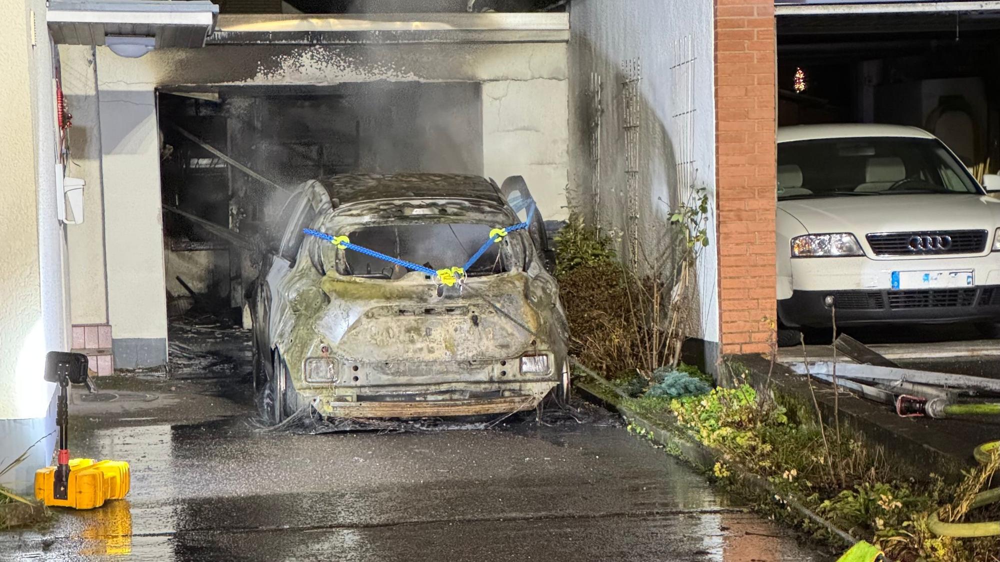 Ein völlig ausgebranntes Elektroauto wird von der Feuerwehr mit einer Seilwinde aus einer Garage am Neuenweg in Bergisch Gladbach gezogen.