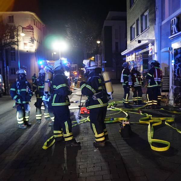 Feuerwehrleute stehen in der Dunkelheit vor dem Gebäude, in dem es gebrannt hat.
