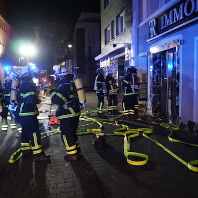 Feuerwehrleute stehen in der Dunkelheit vor dem Gebäude, in dem es gebrannt hat.