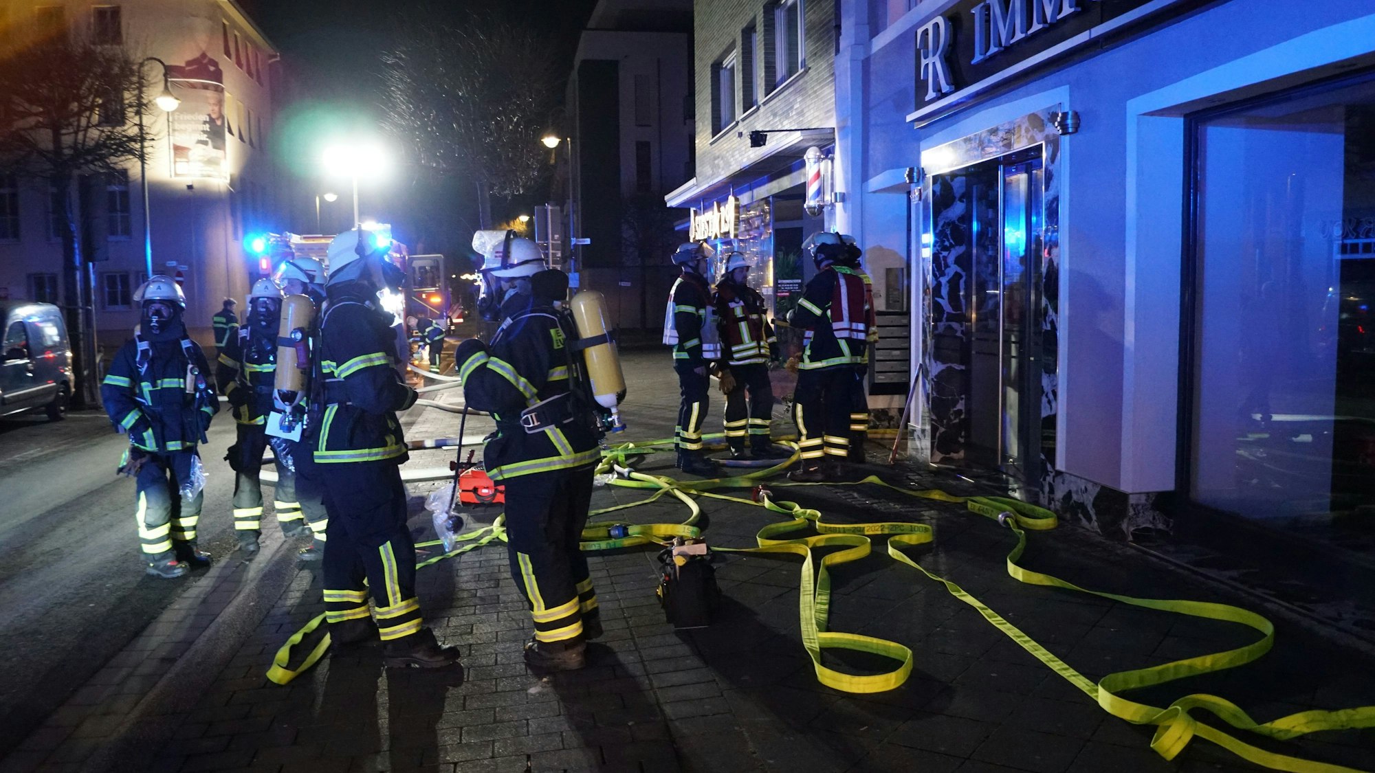 Feuerwehrleute stehen vor dem Haus in der Wilhelmstraße, Schläuche liegen auf dem Boden.