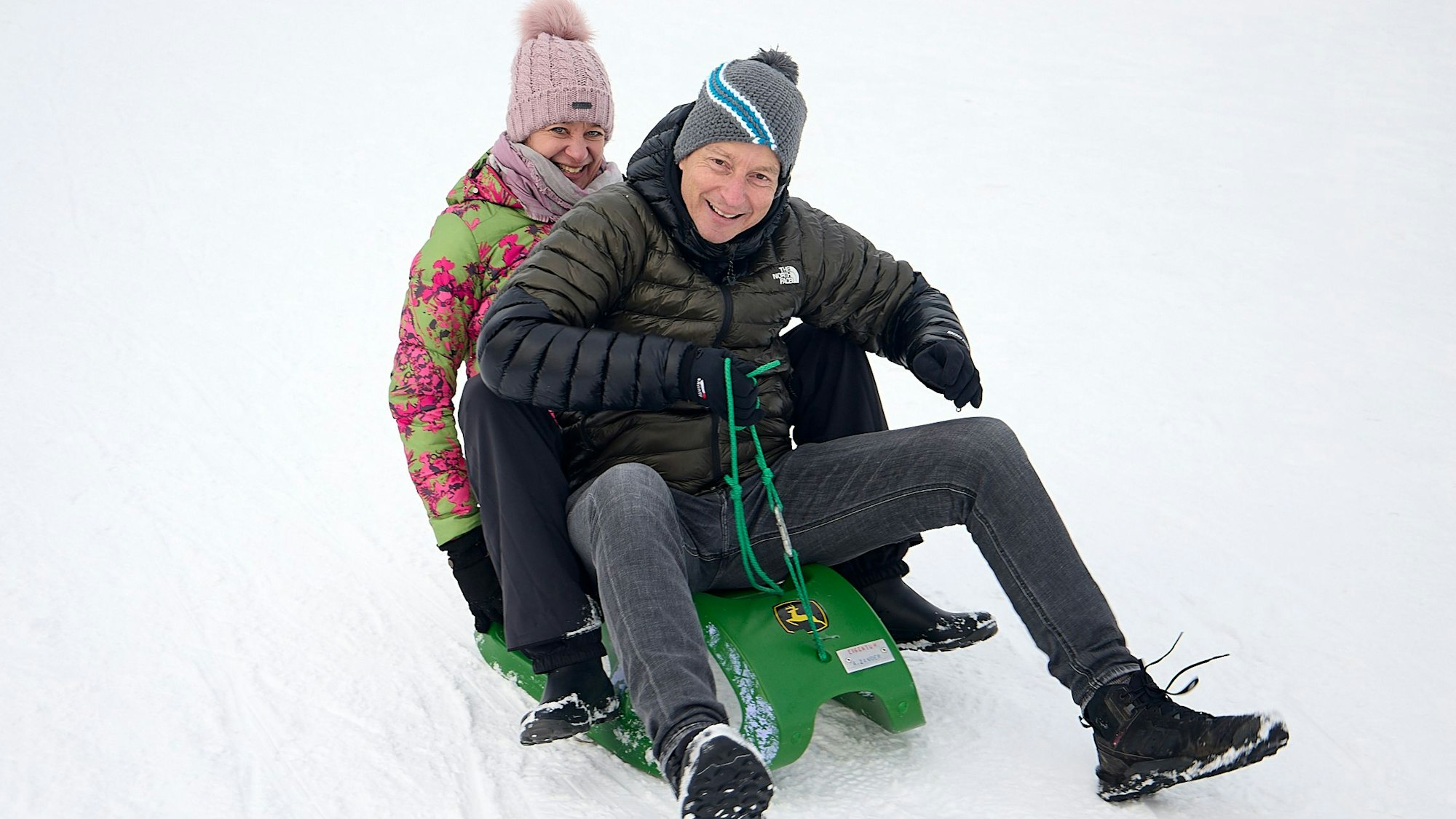 Das Ehepaar rodelt den Hang hinab.