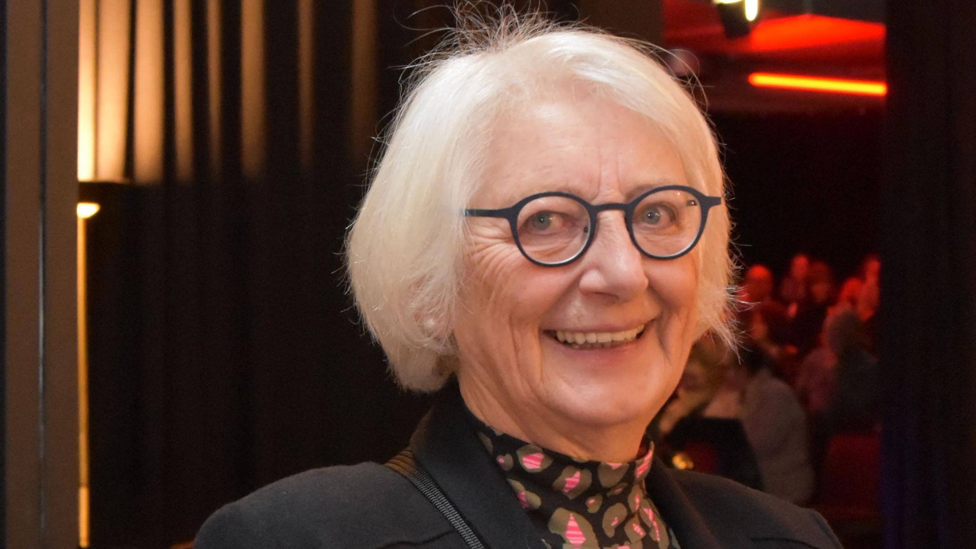 Eine grauhaarige Frau mit runder Brille.