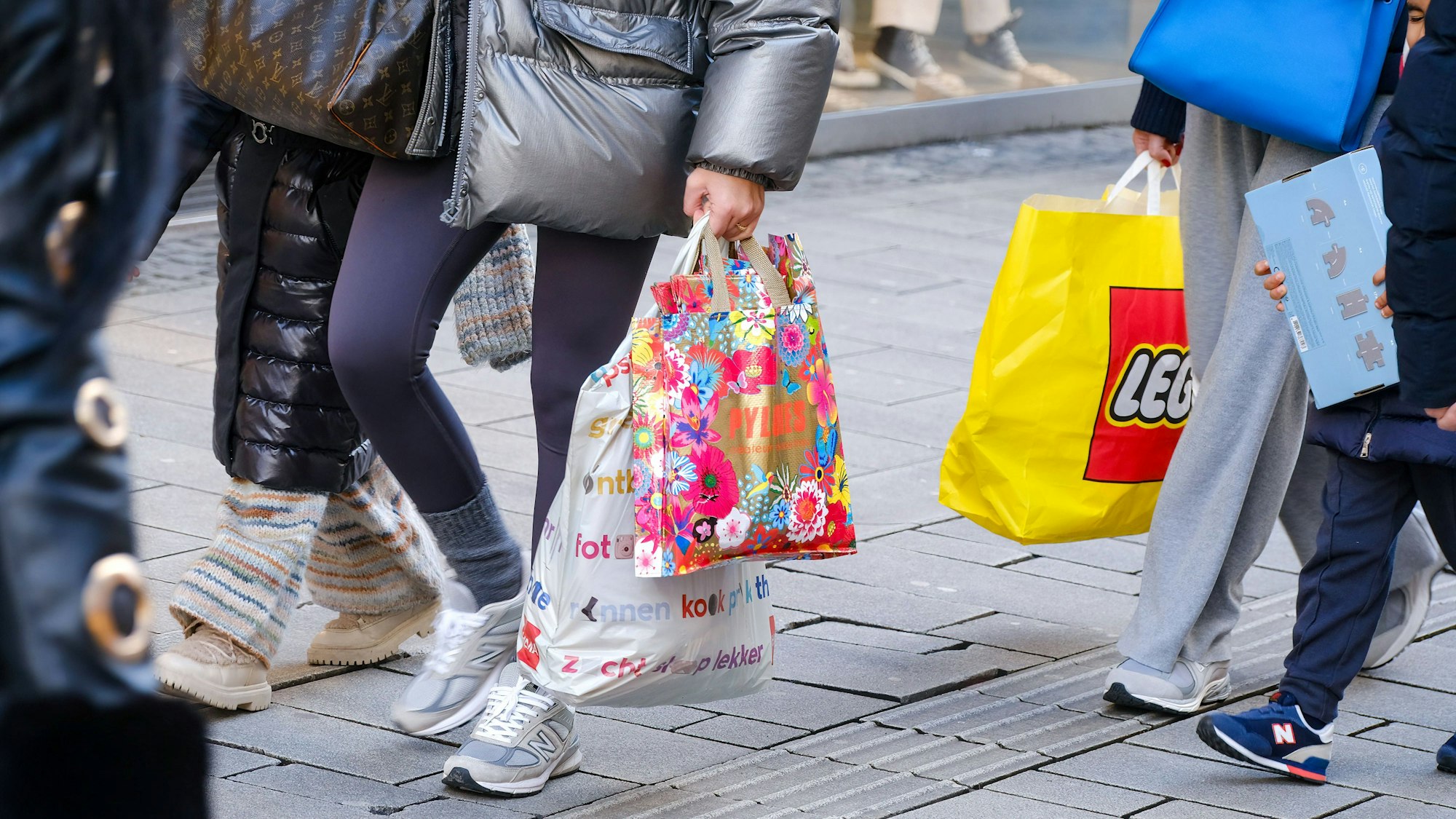 Auf einer Einkaufsstraße laufen Menschen, die Tüten on Läden wie „Lego“ in den Händen halten, entlang.