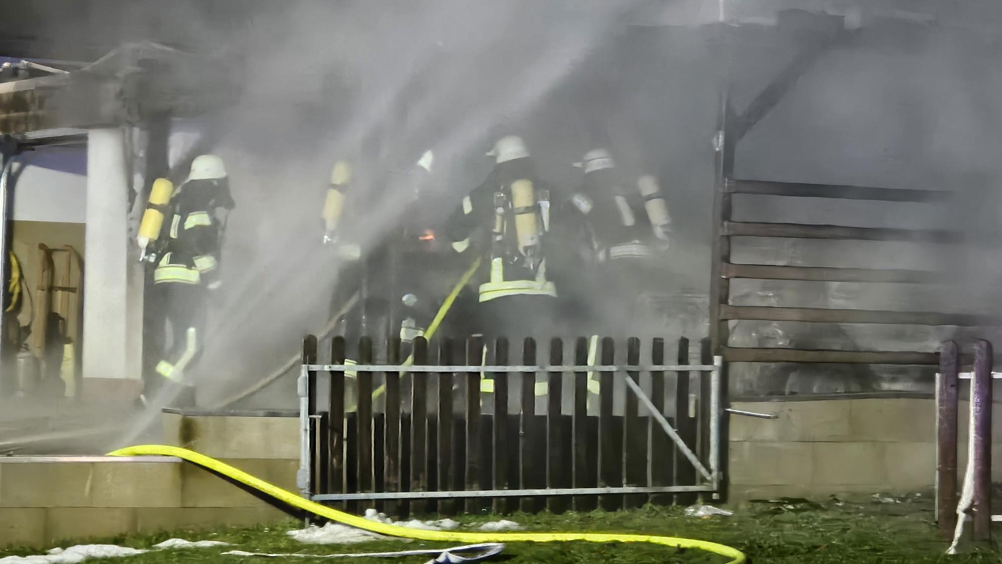 Feuerwehrleute mit Atemschutzausrüstung löschen einen brennenden Carport in Schleiden.