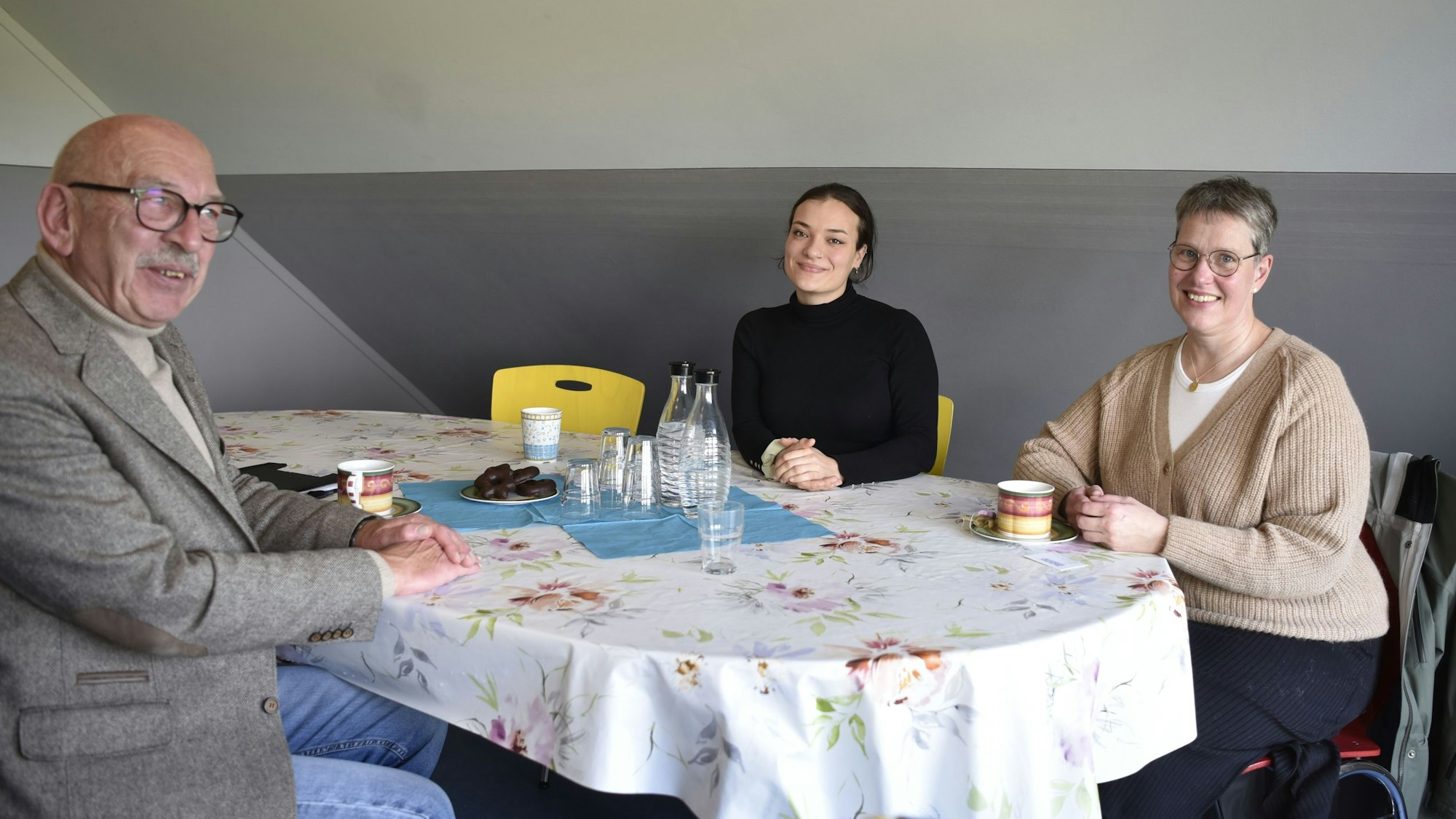 Friedrich Ohst, Alesha Gasior und Astrid Günther sitzen an einem Tisch mit geblümter Tischdecke.