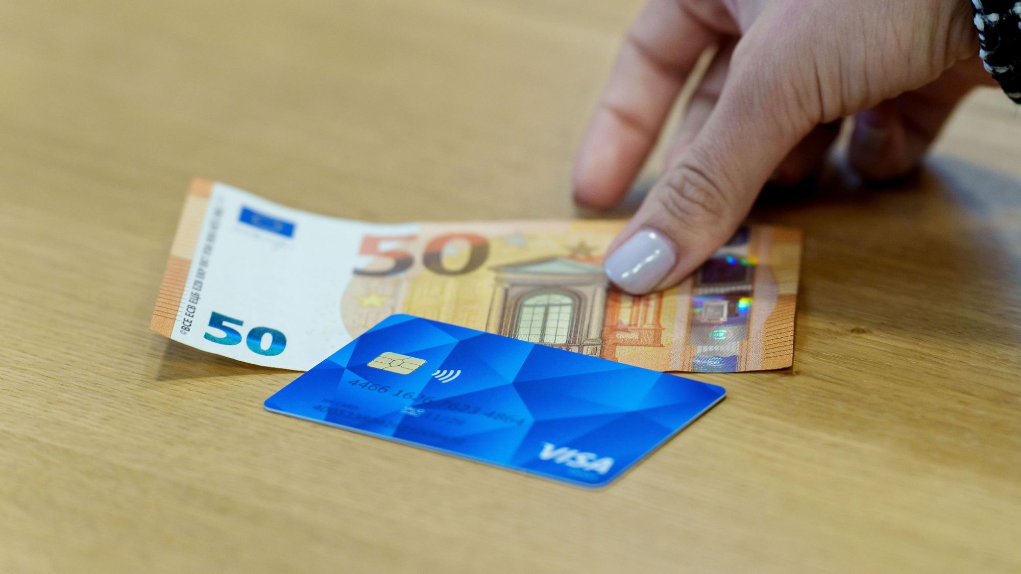 Die Bezahlkarte für Asylbewerberinnen und Asylbewerber und ein 50 Euro Schein liegen nebeneinander.