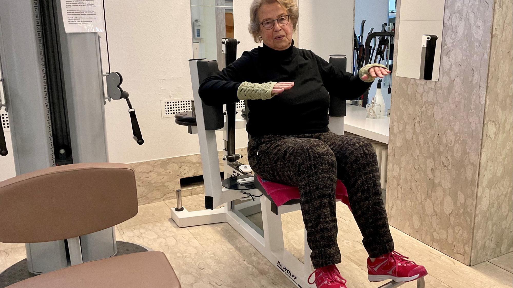 Eine ältere Frau sitzt auf einem Fitnessgerät.