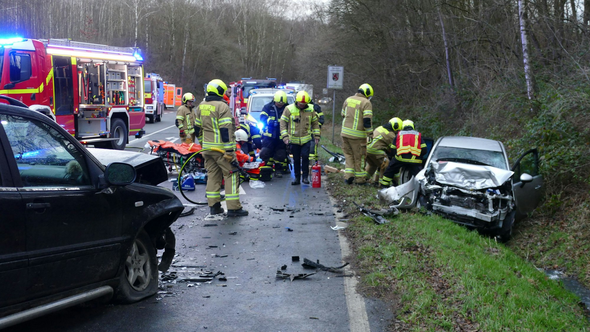 Ein Unfallwagen liegt in einem Graben, die Straße ist mit Trümmerteilen übersät. Einsatzkräfte der Feuerwehr und Polizei sind auf der Straße.