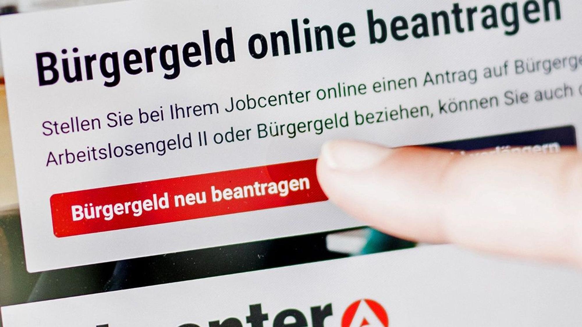 Eine Frau tippt auf einem Tablet auf einen Link zum Beantragen des Bürgergeldes im Kundenbereich in einem Jobcenter.