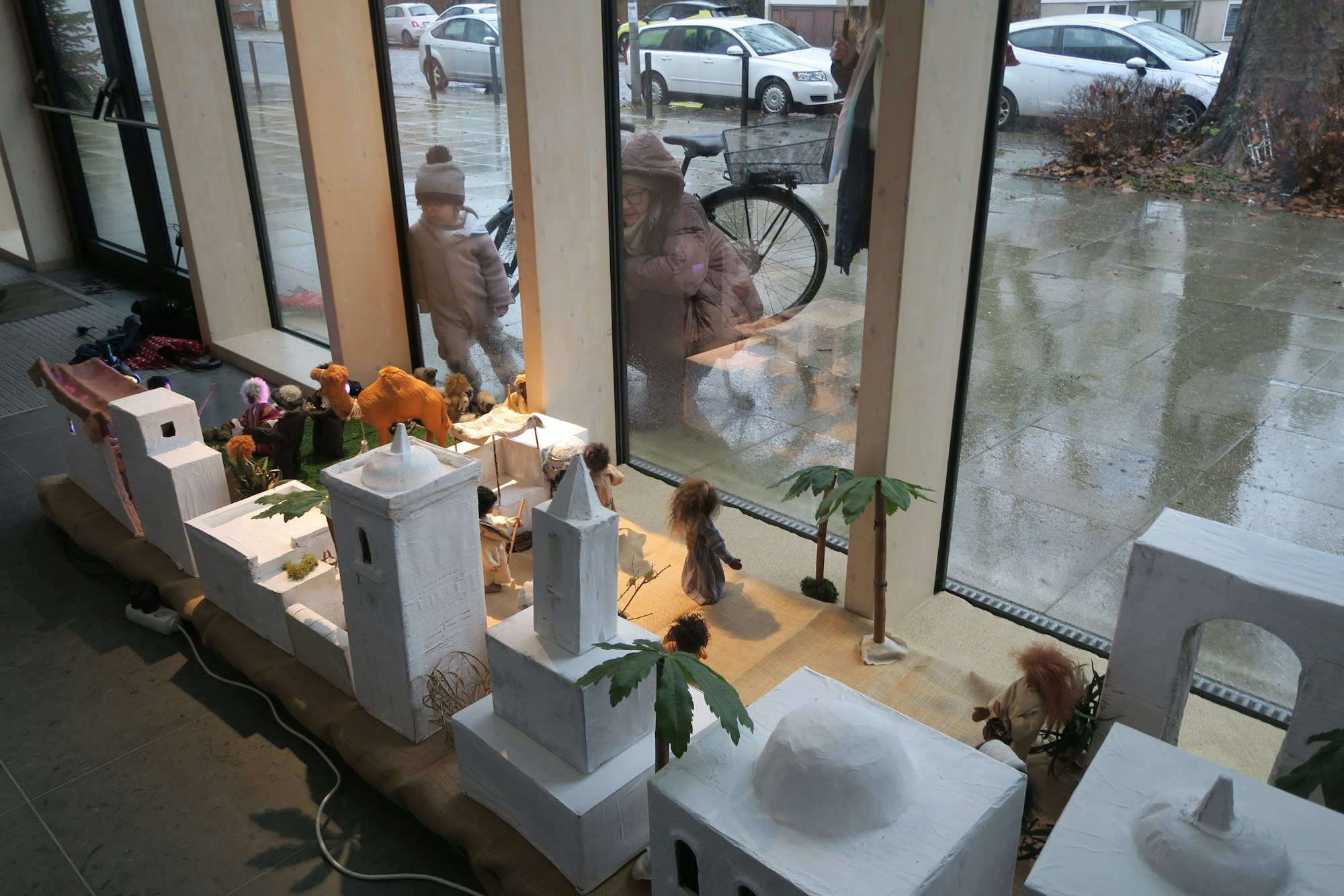 Durch bodentiefe Fenster betrachten eine Mutter und ein Kind die Krippe in der Kirche St. Epiphanias.