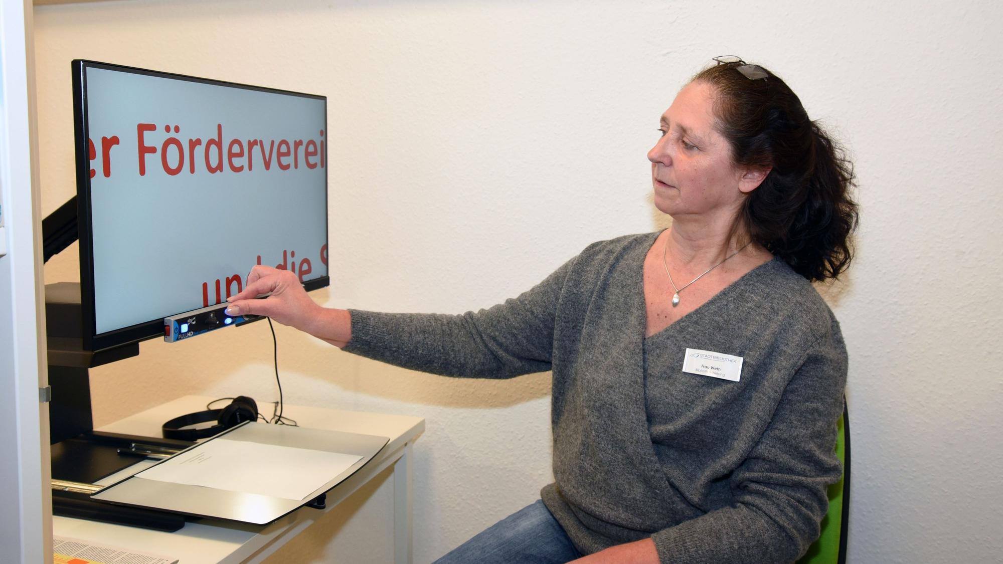 Eine Frau führt ein Lesegerät an einem Computer vor, das Buchstaben vergrößert.