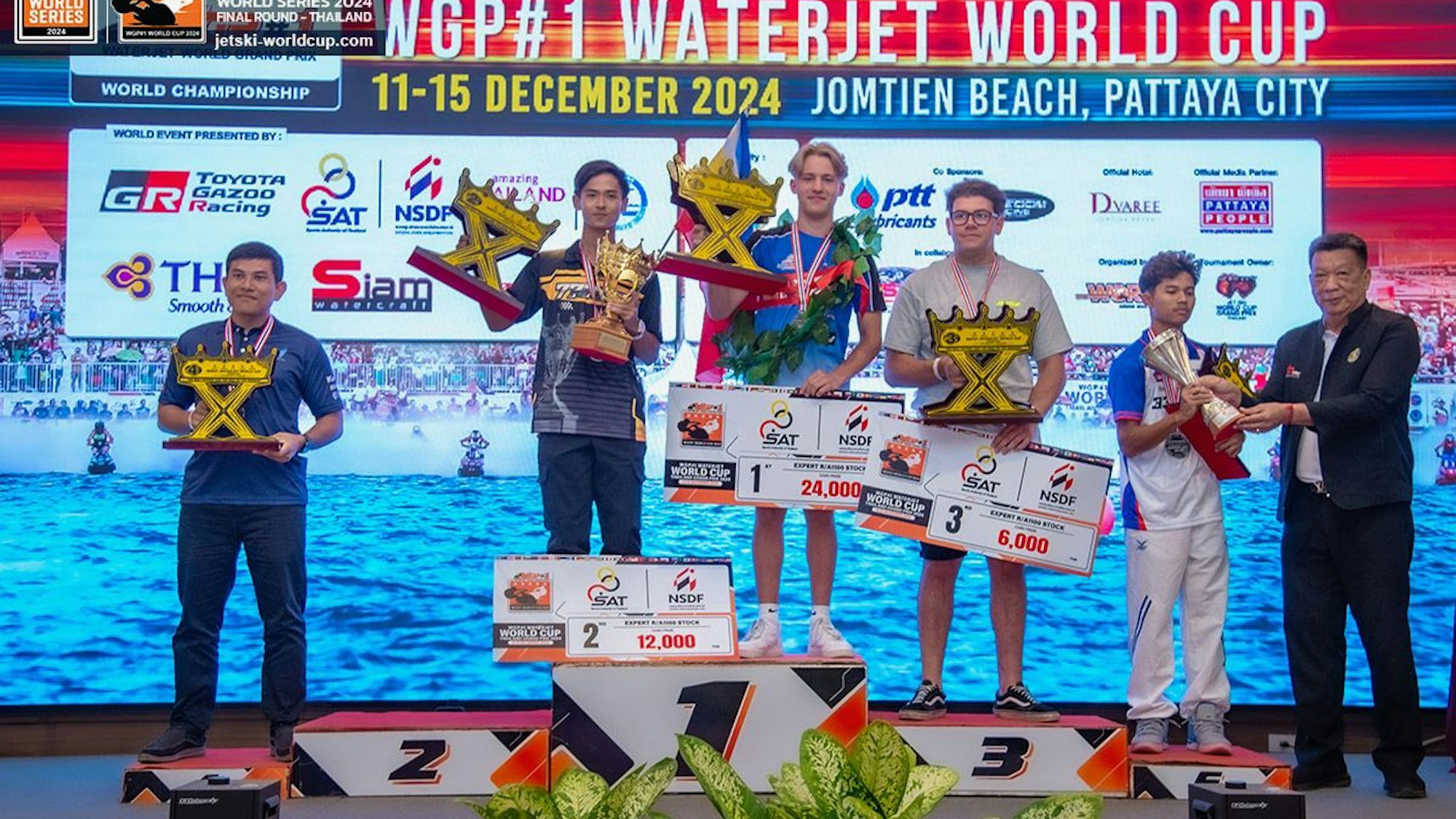 Auf dem Bild ist eine Siegerehrung mit Podest, Pokalen und mehreren Männern zu sehen.