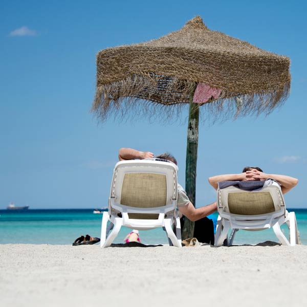 Zwei Menschen sitzen unter einem Sonnenschirm am Strand.