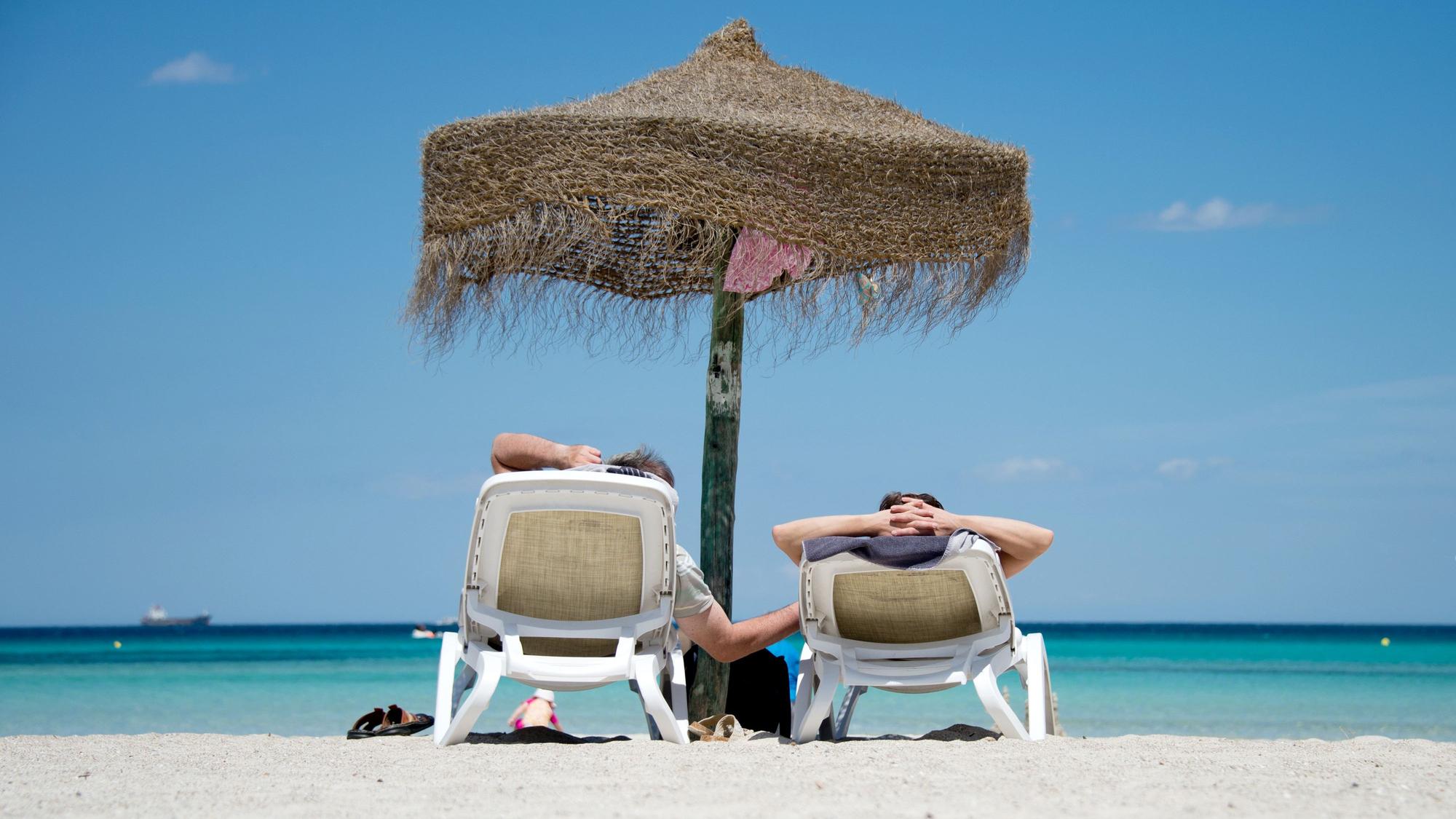 Zwei Menschen sitzen unter einem Sonnenschirm am Strand.