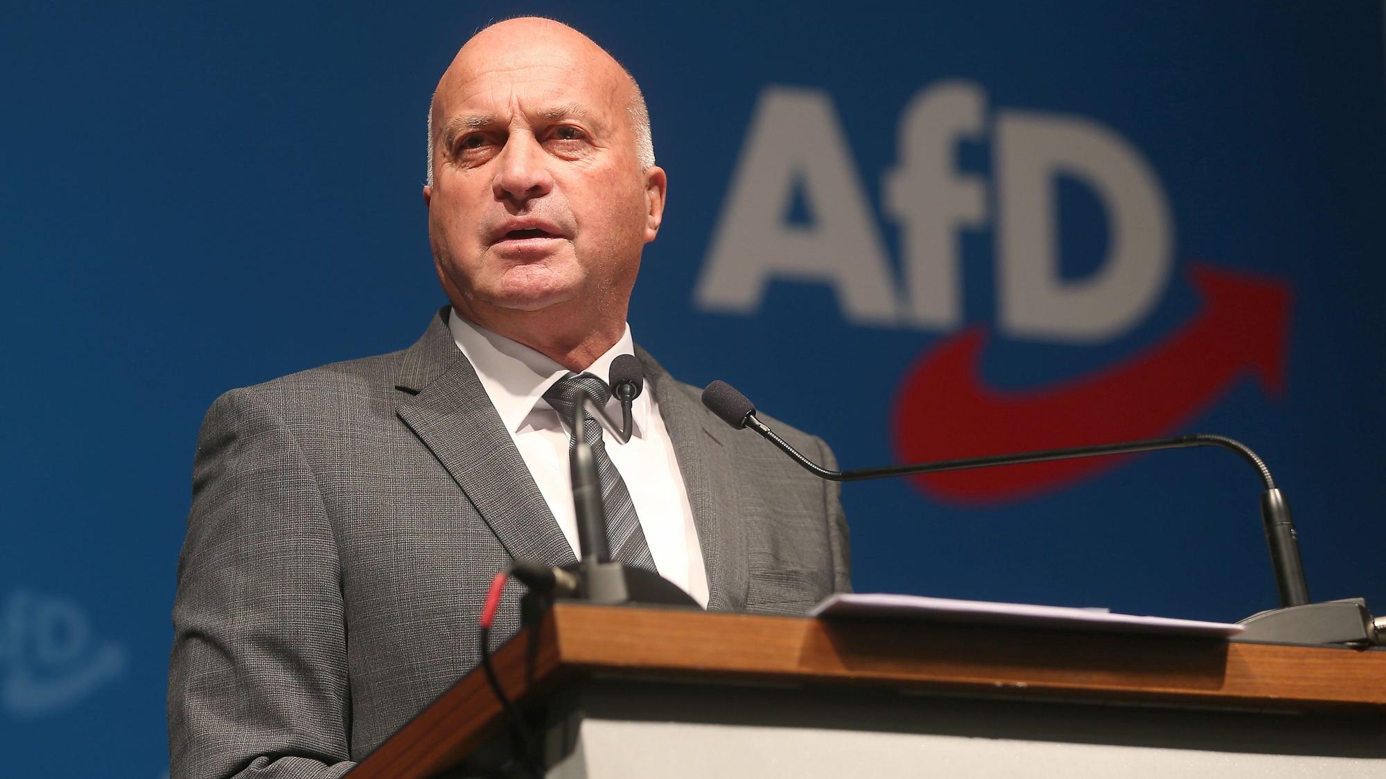 Rüdiger Lucassen steht an einem Rednerpult, auf einer Wand dahinter steht das AfD-Logo.