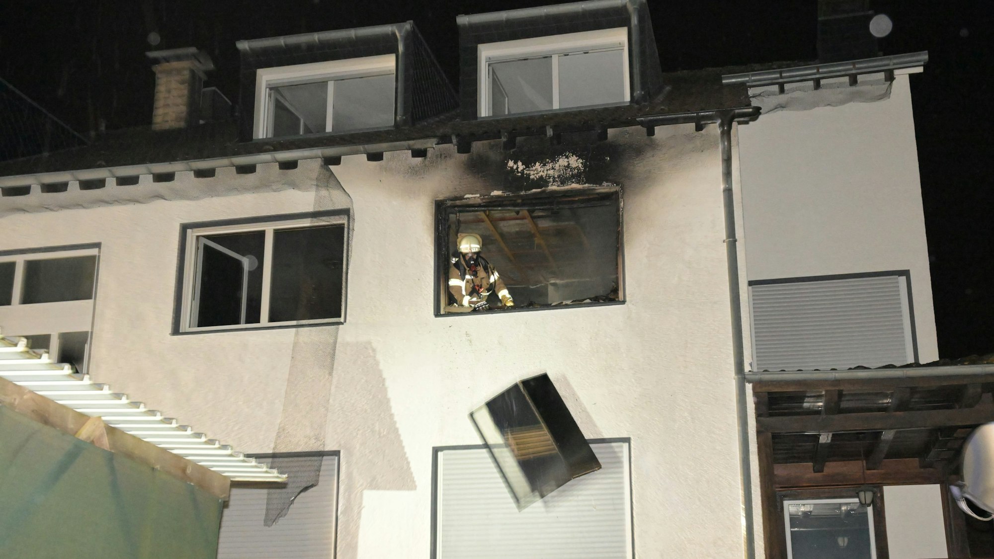 Ein Feuerwehrmann wirft ein Möbelstück aus einem Fenster im Obergeschoss eines Mehrfamilienhauses.