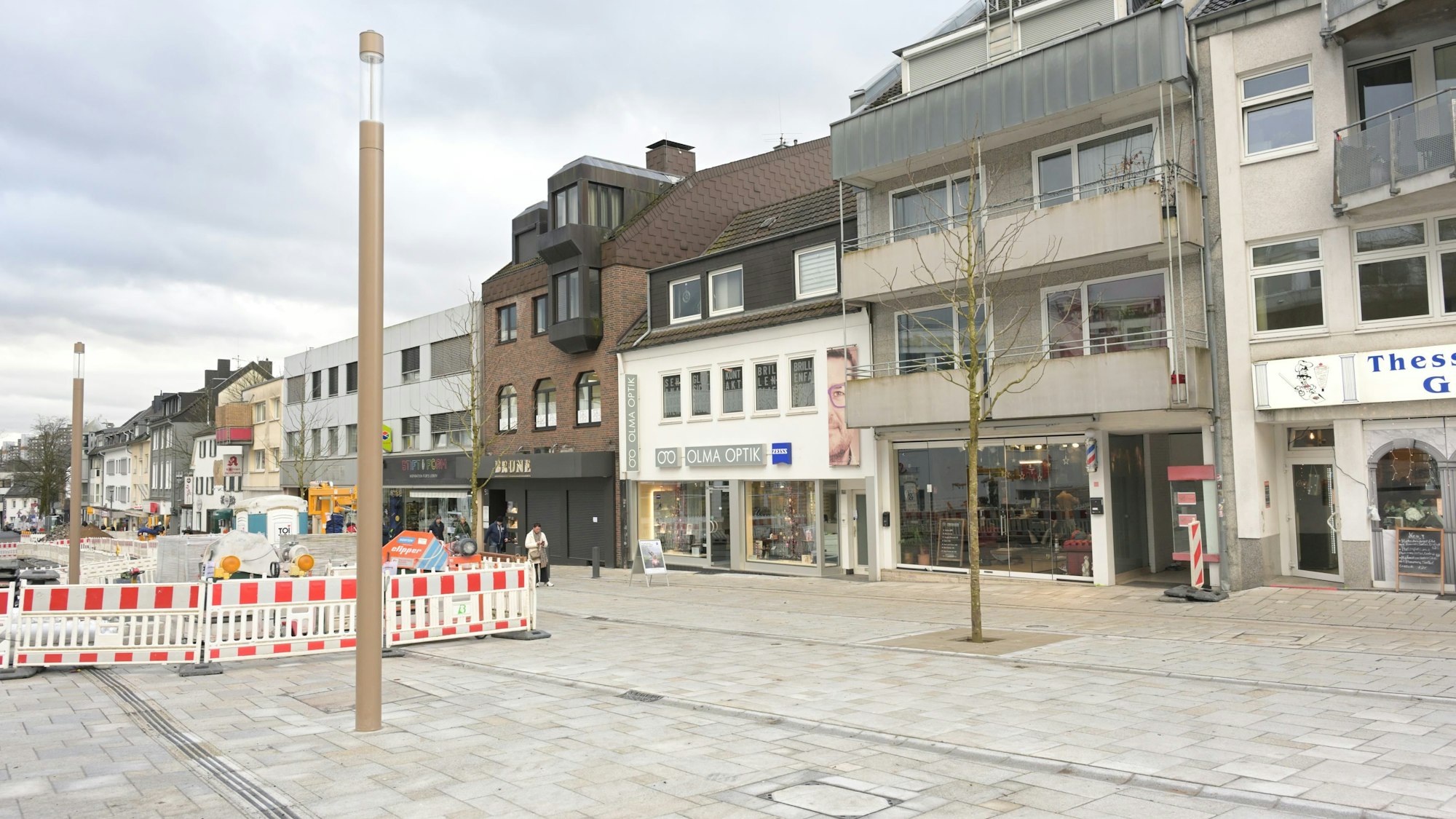 Geschäfte, die Baustelle in der Mitte der Straße sowie das neue Granitpflaster sind zu sehen.