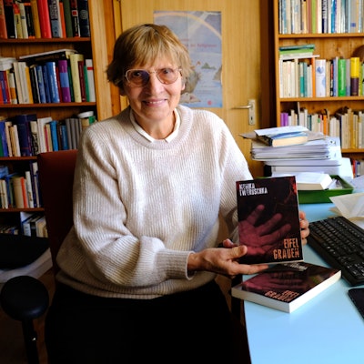 Die Autorin Monika Tworuschka aus Arloff sitzt am Schreibtisch ihres Arbeitszimmers und hält ihren ersten Kriminalroman „Eifel-Grauen“ in die Kamera.