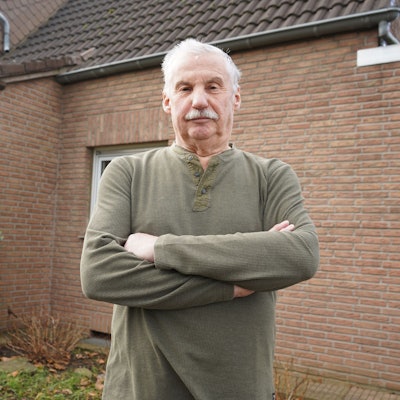 Das Foto zeigt einen Mann mit verschränkten Armen vor einem Haus.