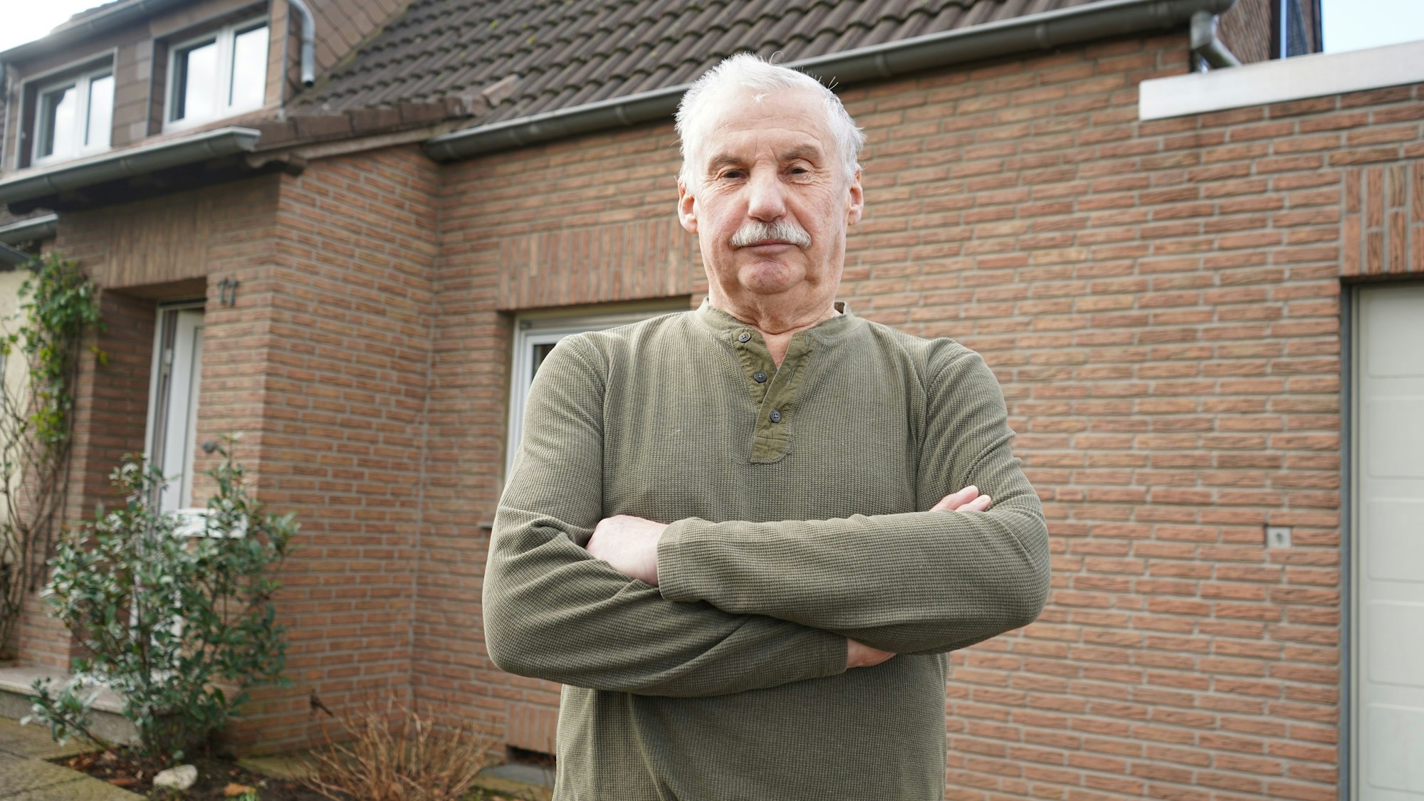 Das Foto zeigt einen Mann mit verschränkten Armen vor einem Haus.