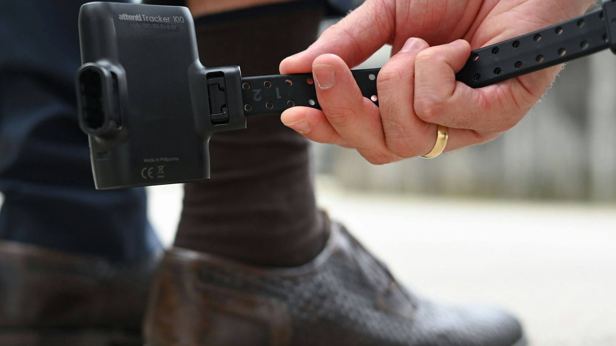 Ein Mann hält eine elektronische Fußfessel an sein Bein.