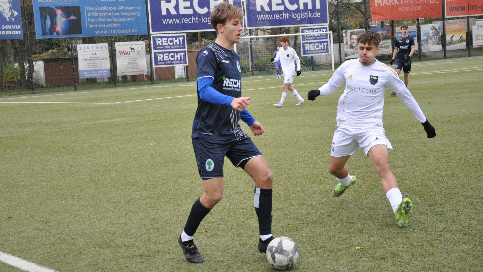 Das Foto zeigt zwei Fußballer im Zweikampf, der blau gekleidete Königsdorfer schirmt den Ball vor dem Gegner ab.