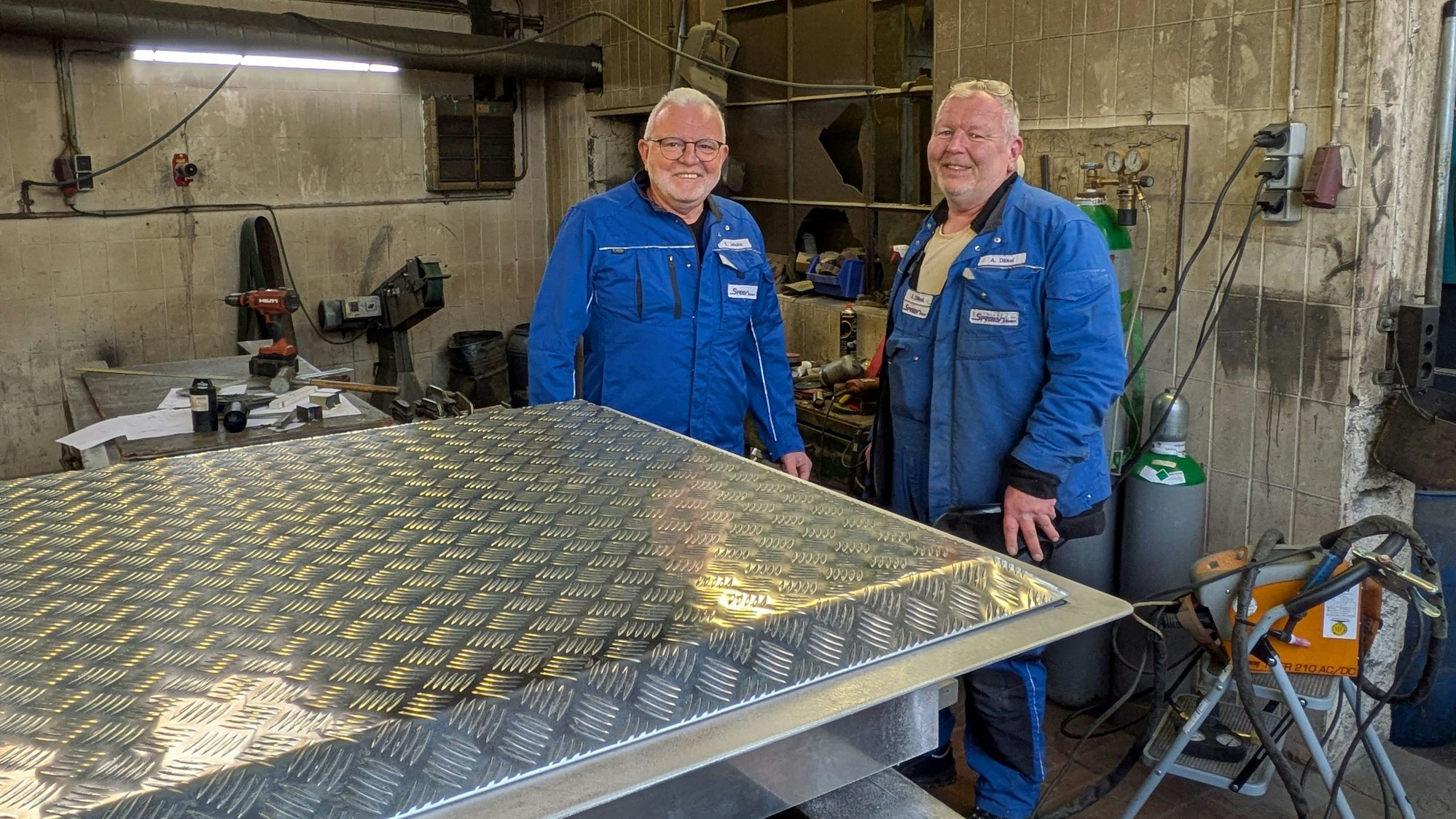 Zwei Männer stehen in einer Schlosserei-Werkstatt.