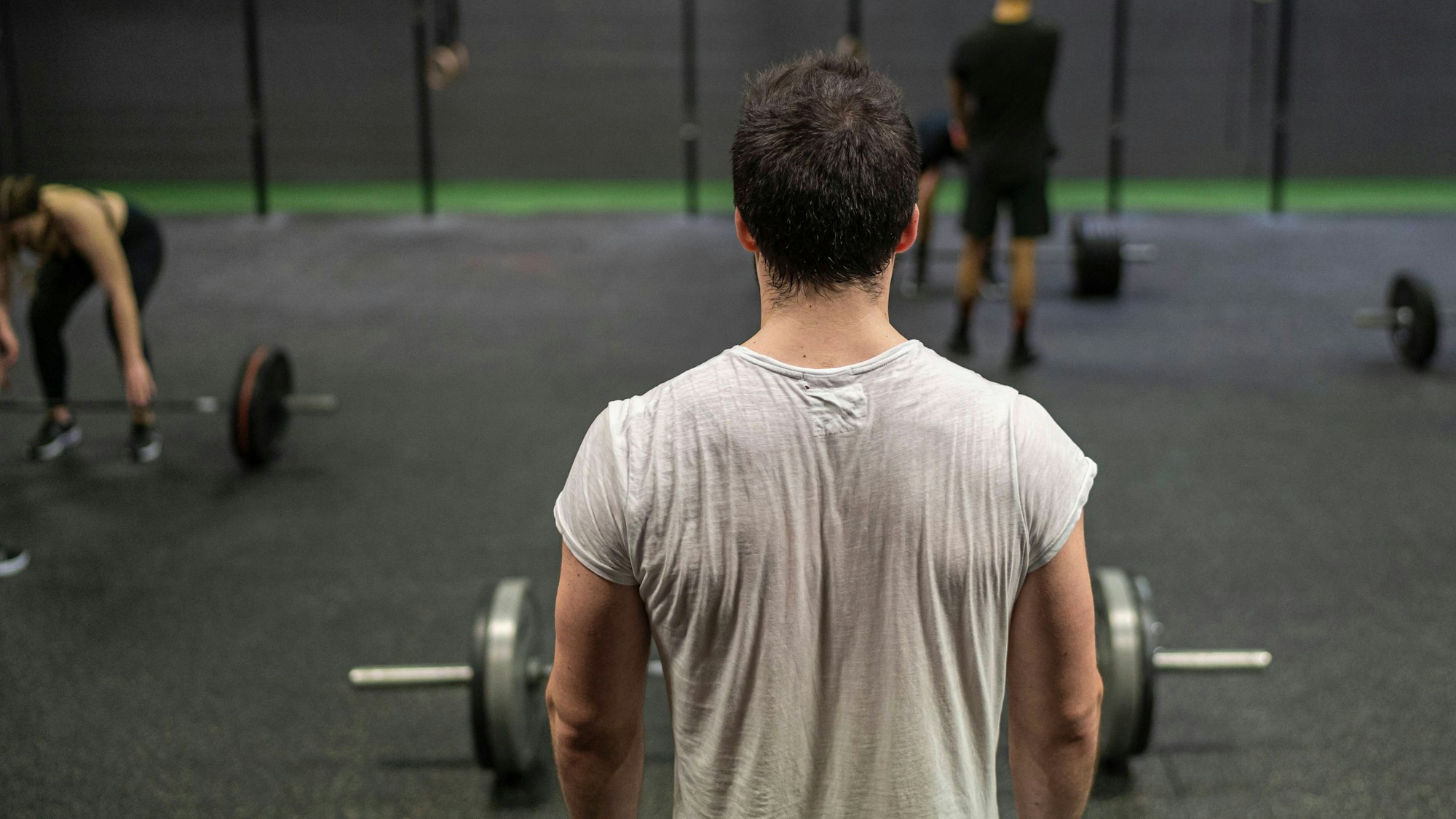 Ein Mann steht mit dem Rücken zur Kamera bei einem Fitnesskurs vor einer Langhantel.